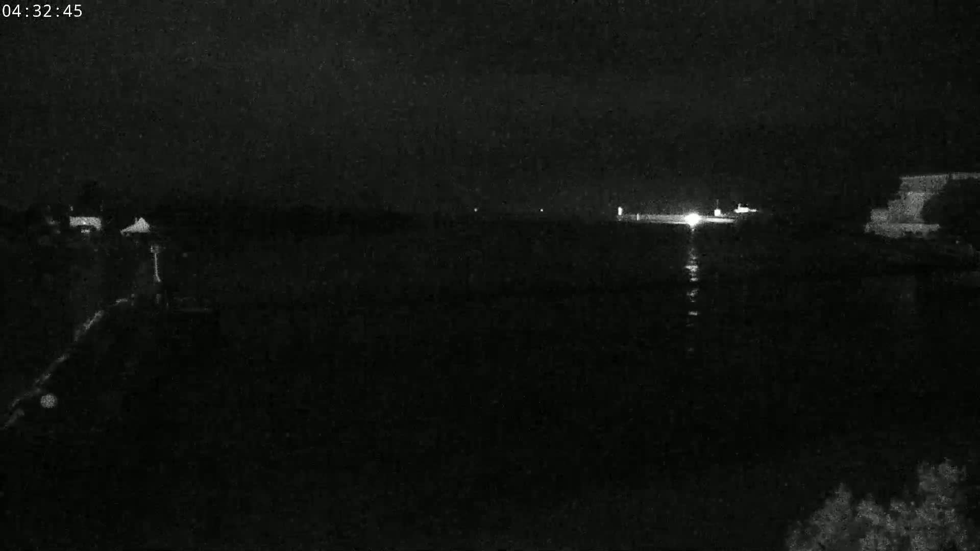 A dark, nighttime scene shows a body of water reflecting a few distant lights under a mostly clear sky.