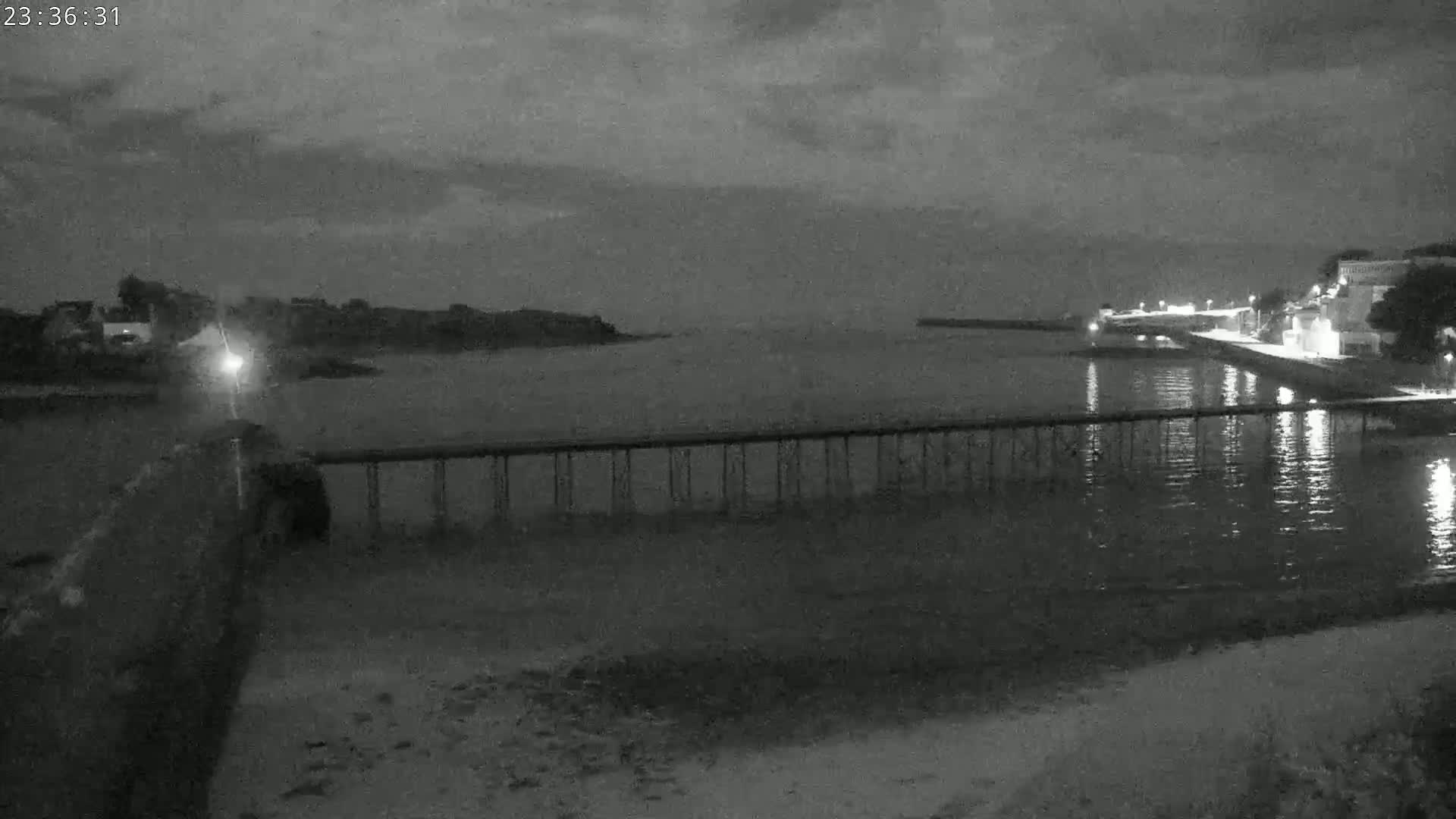 A long pier extends over dark water at night under a cloudy sky.