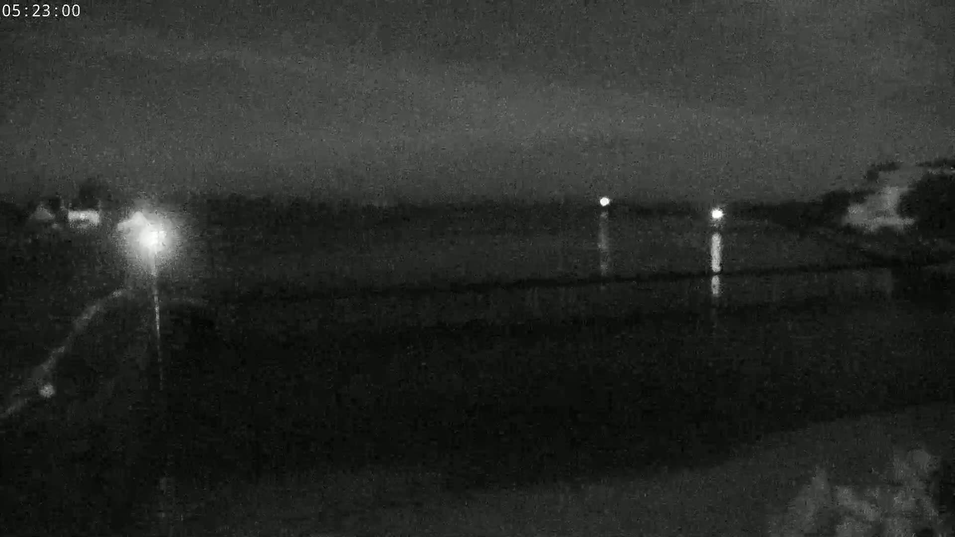 A nighttime view of a dark body of water with faint lights reflecting on its surface and a light source visible in the distance on the left.