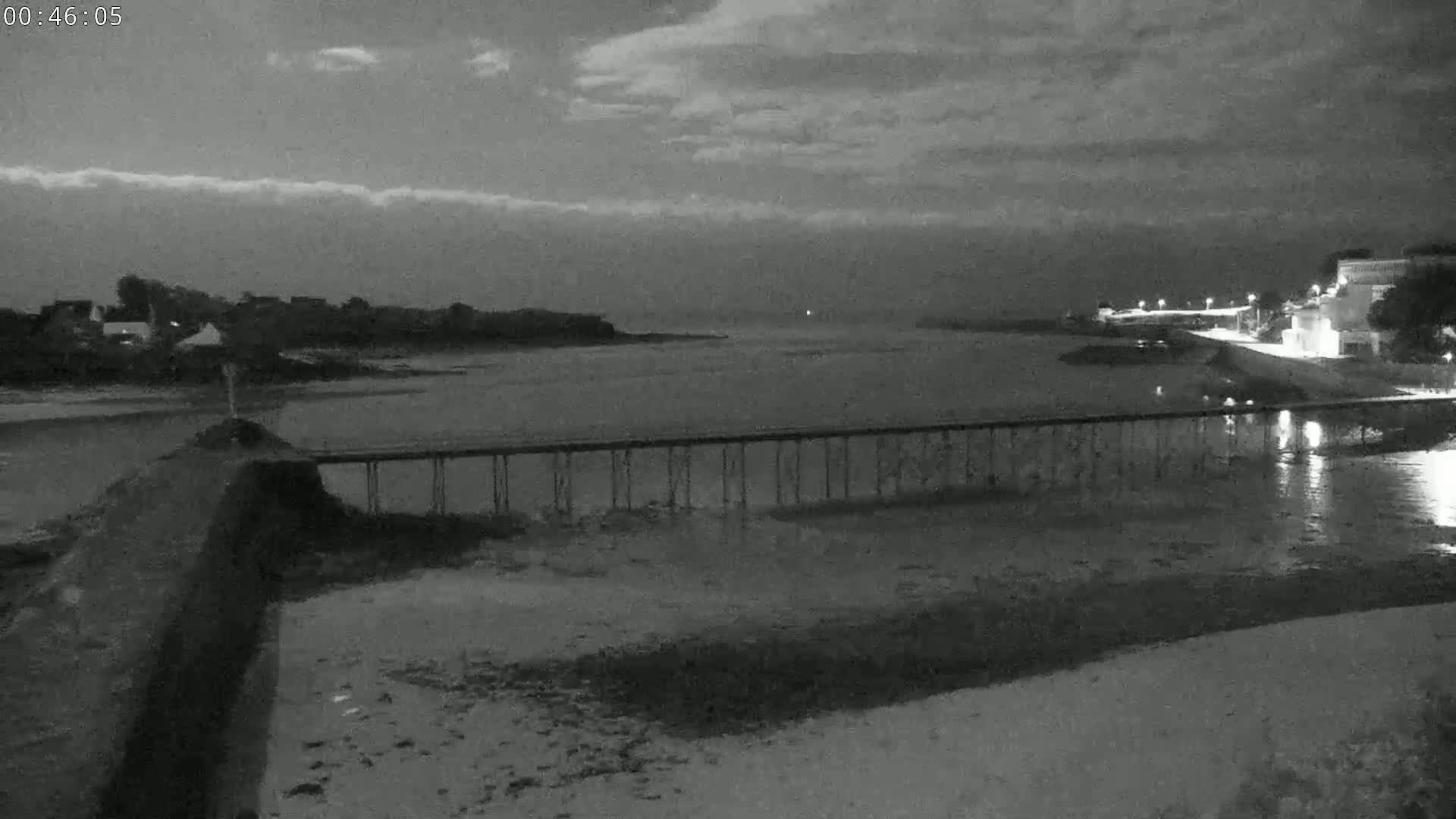 A long pier stretches across a calm, dark body of water under a cloudy night sky.