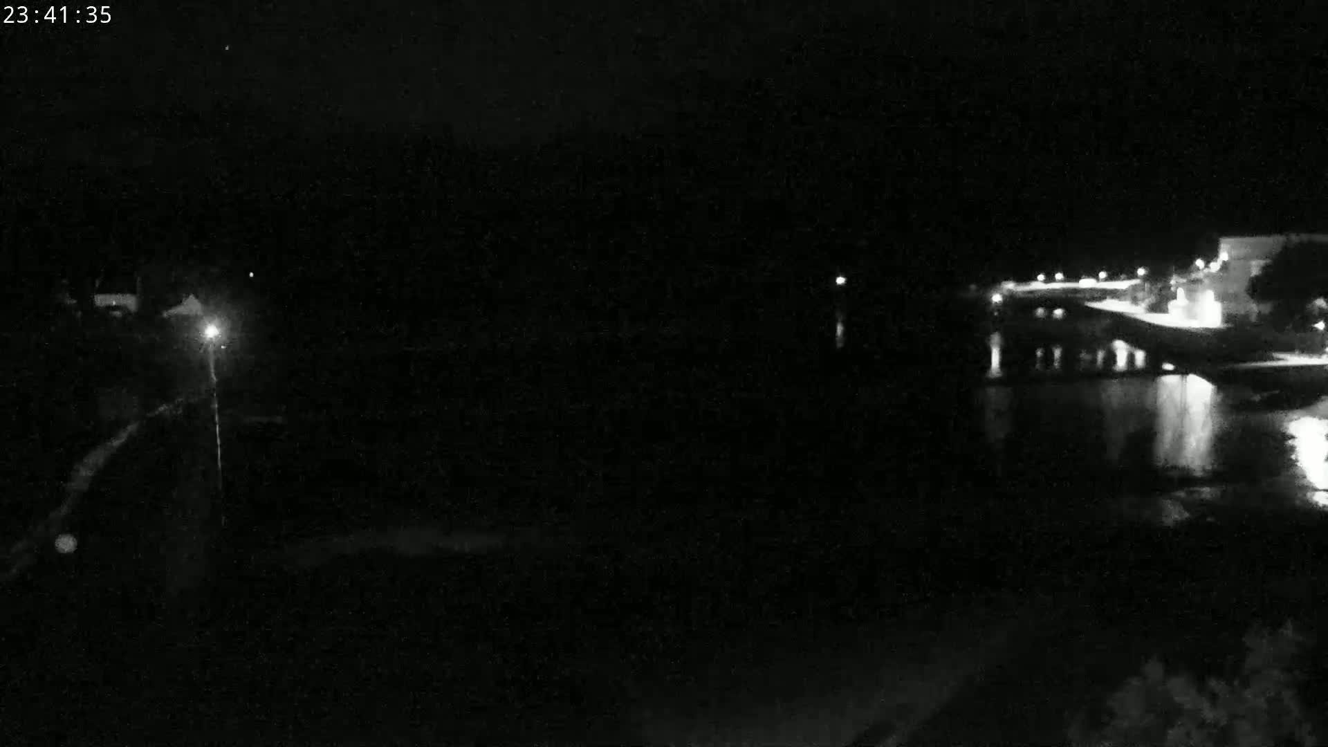 A nighttime, low-light view shows a dark body of water reflecting lights from a distant shoreline.