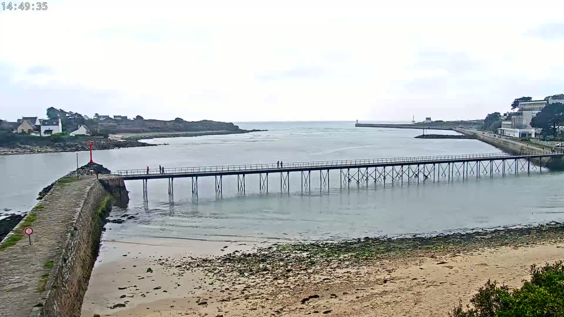A long pier extends over calm, gray water toward a small town under an overcast sky.