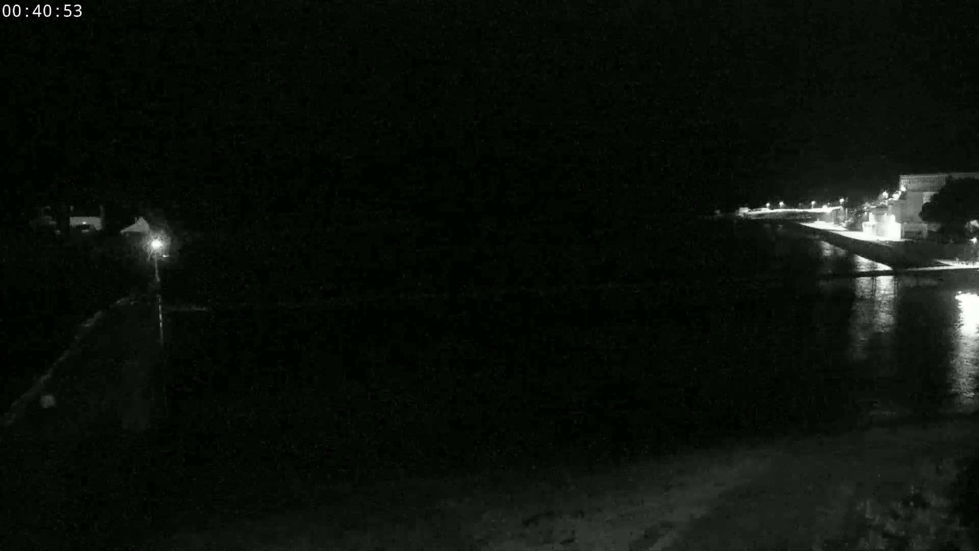 A nighttime, low-light view of a dark body of water next to a dimly lit shoreline with buildings.