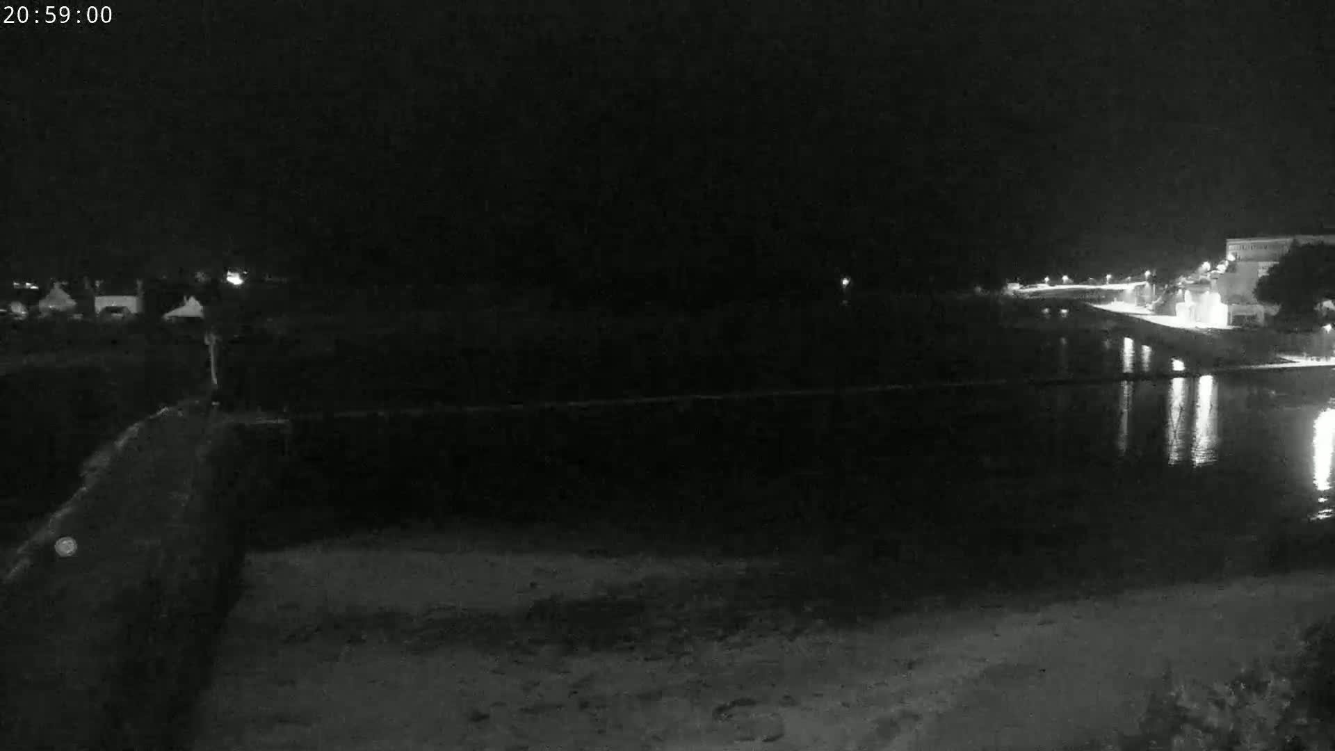 A nighttime, low-light image shows a dark body of water reflecting lights from a distant shoreline.