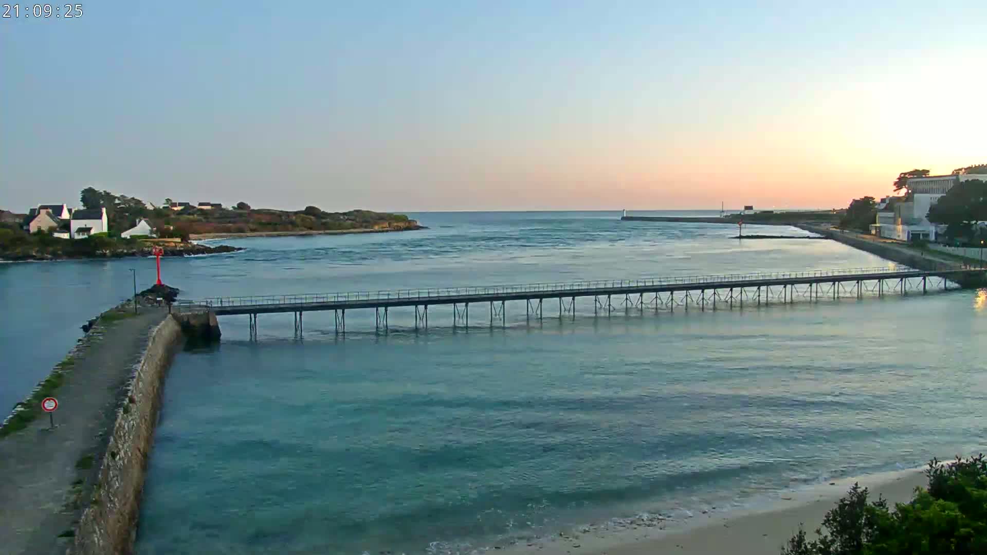 A long pier stretches across a calm body of water at sunset, with buildings and land visible on either side.