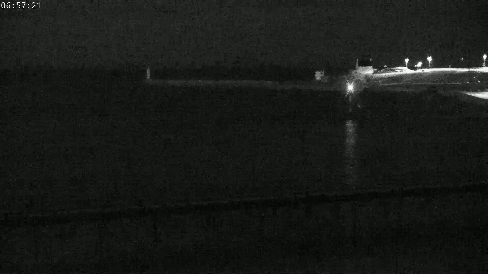 A nighttime, low-light image shows a dark body of water reflecting lights from a distant, dimly lit shoreline.