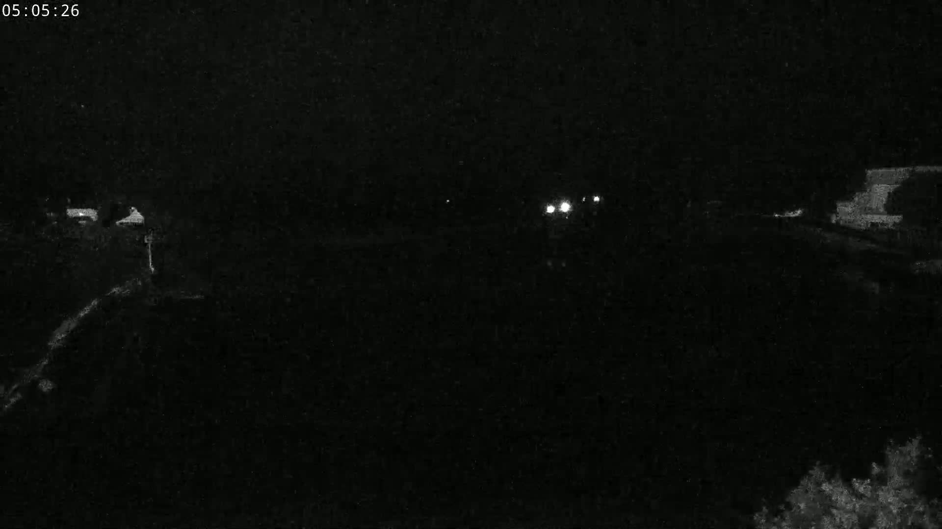 A nighttime, low-light view of a dark body of water with faint lights visible in the distance and some indistinct shapes along the shoreline.