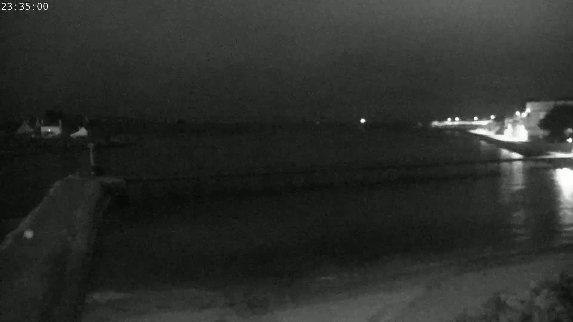 A nighttime, low-light view shows a dark body of water reflecting lights from a distant shoreline.