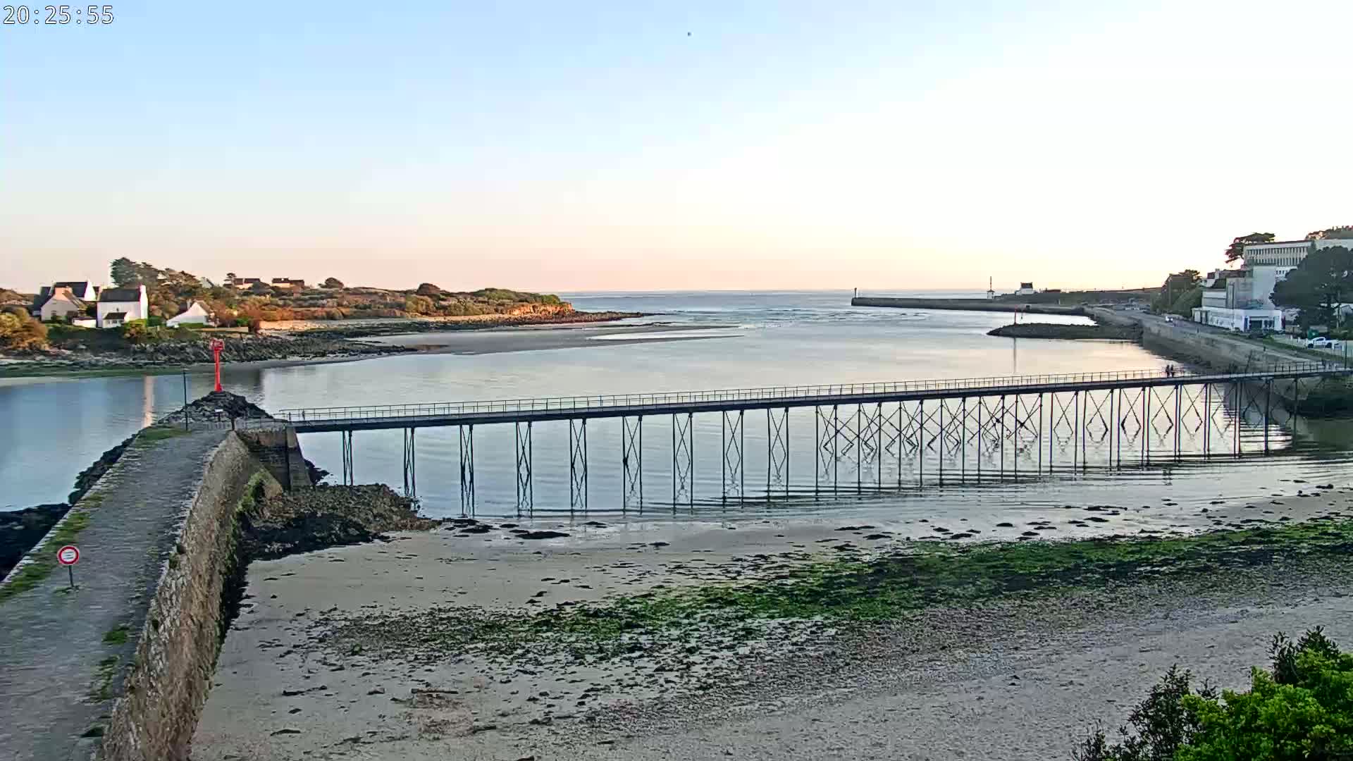 A long pier extends over calm water toward a small town under a clear, light-blue sky.