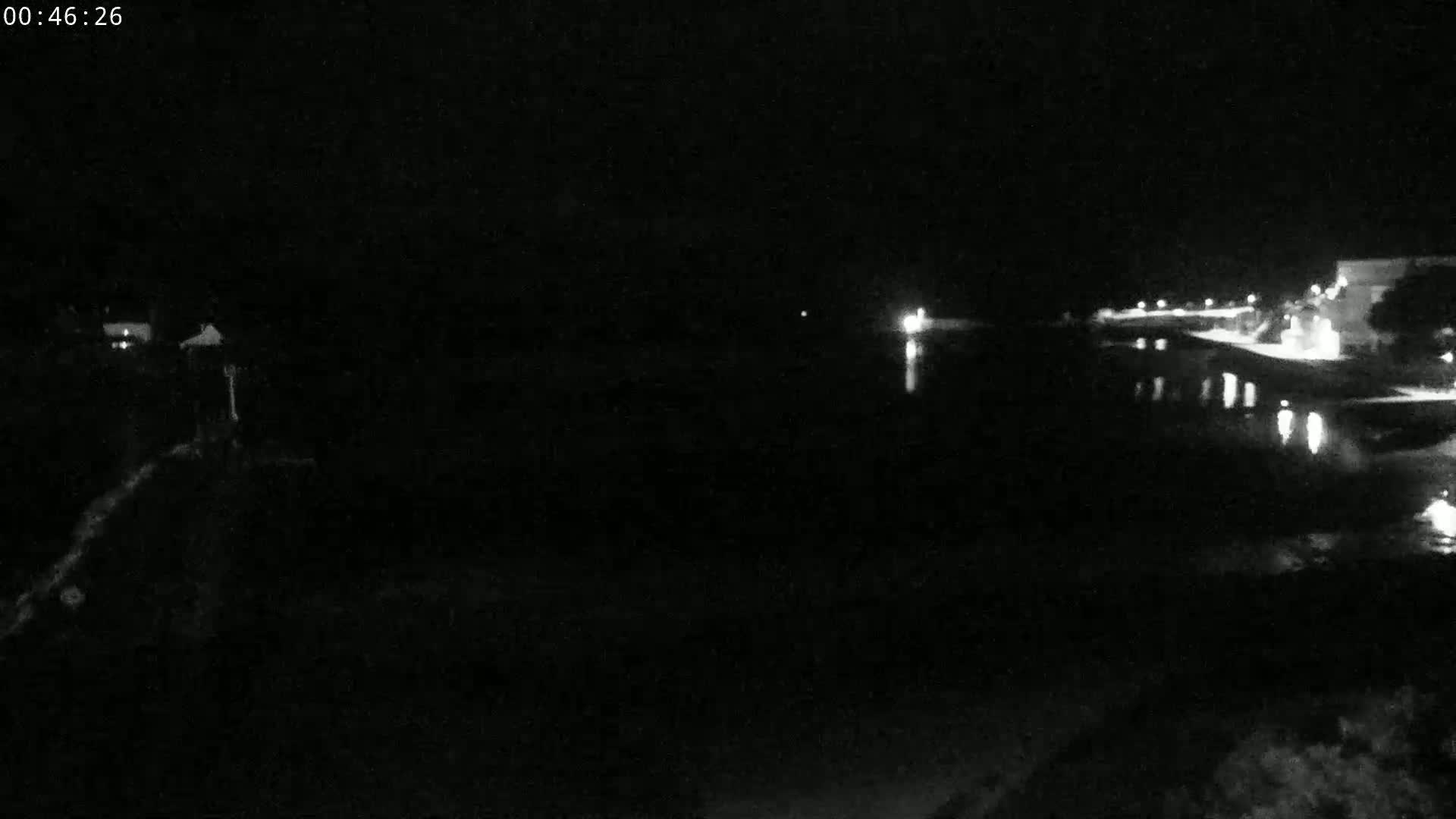 A nighttime view of a dark body of water reflecting a few lights from buildings on the opposite shore.