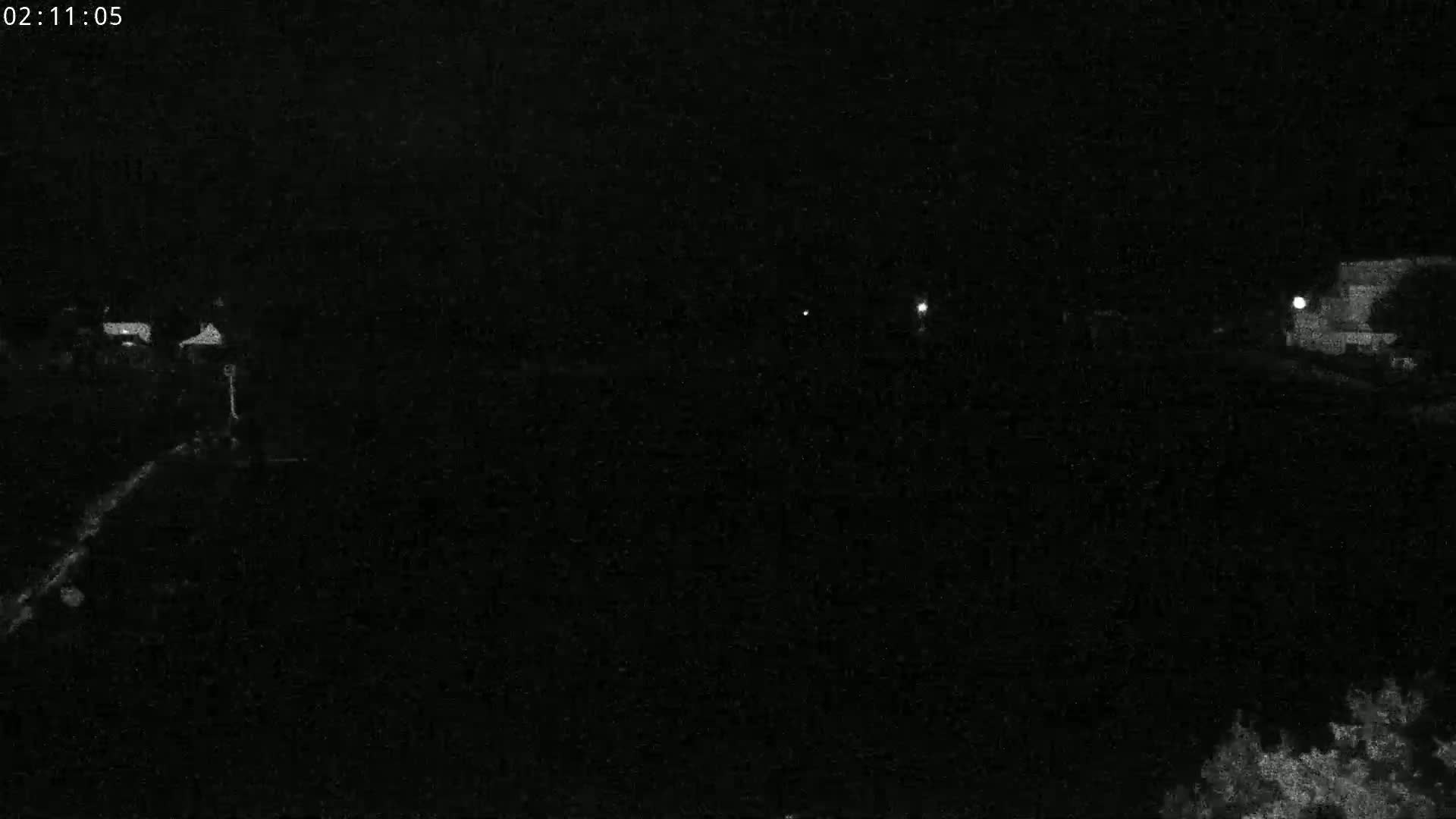 A nighttime, low-light view shows a dark landscape with a few faint lights visible in the distance.
