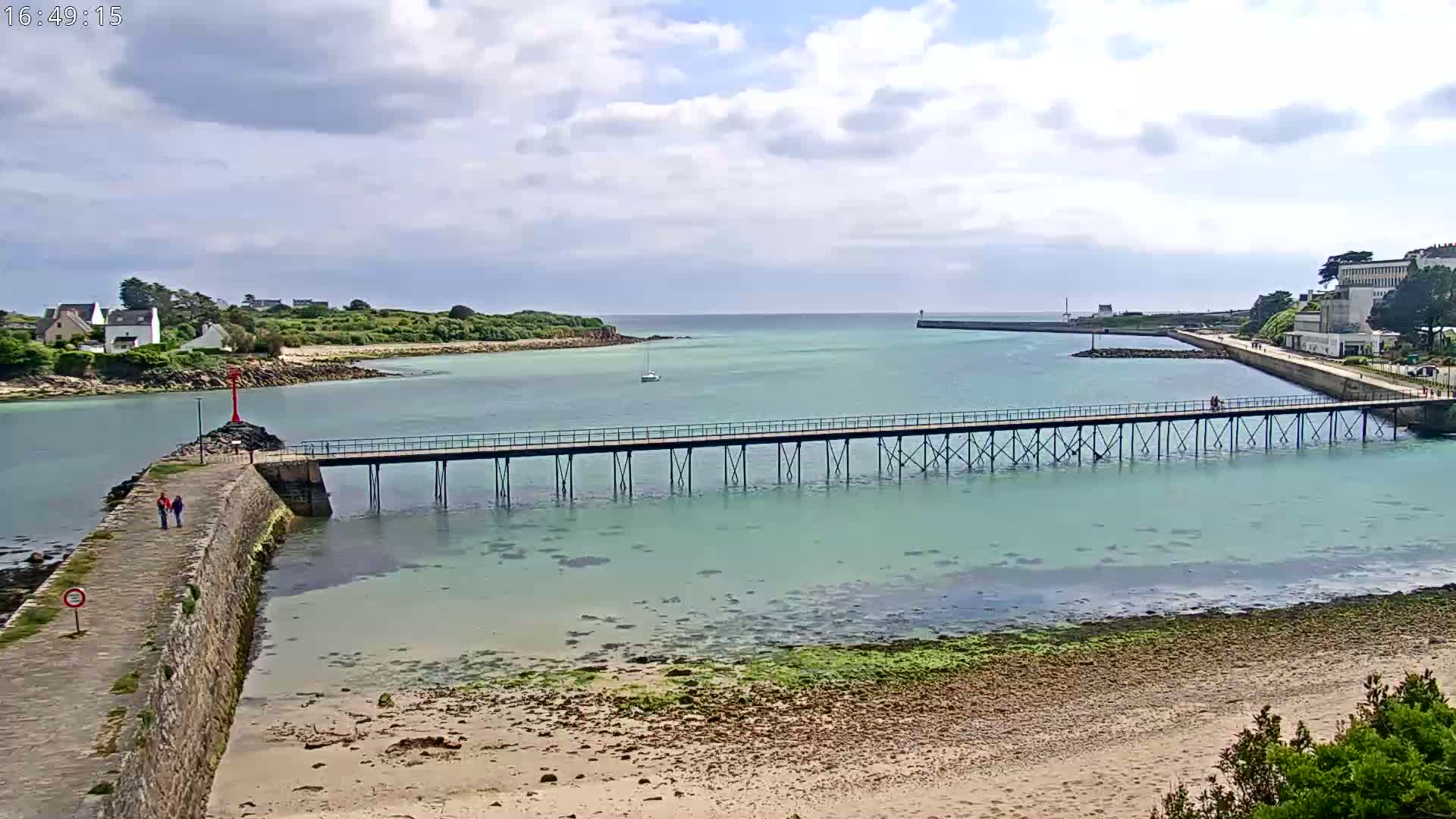 A long pier stretches across calm, light-green water toward a small island under a partly cloudy sky.