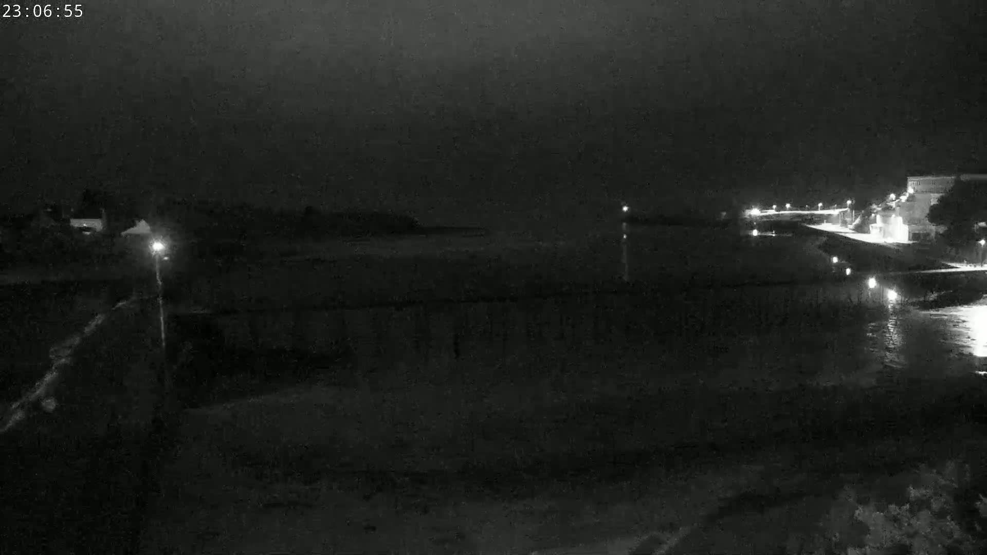 A nighttime, low-light view of a calm body of water with a shoreline featuring buildings and lights.
