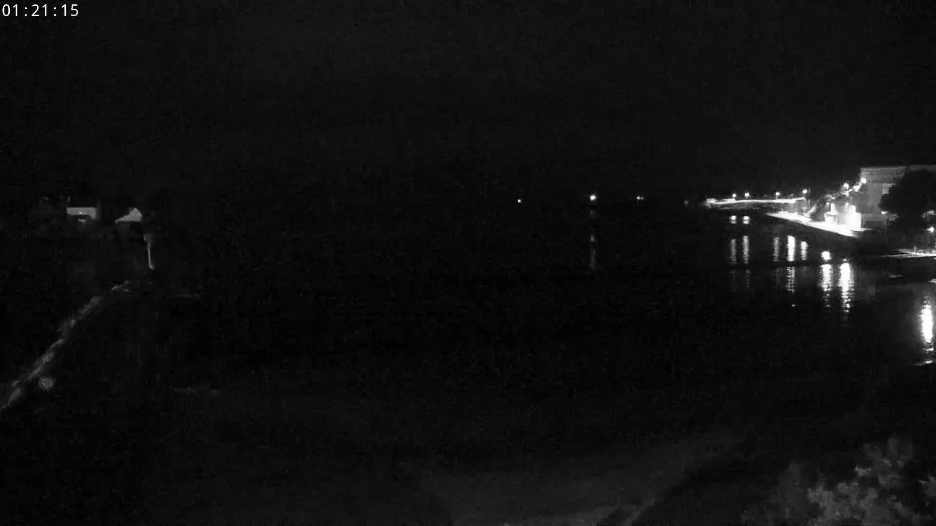 A nighttime, low-light view of a calm body of water reflecting lights from a distant shoreline.