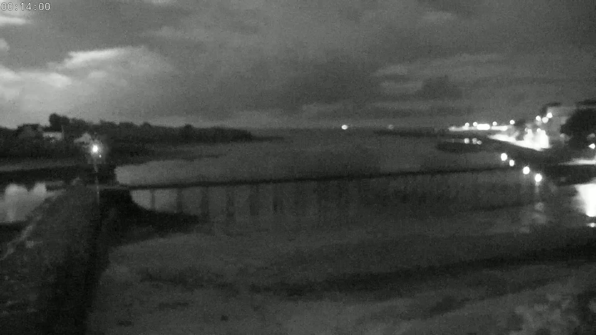 A nighttime, overcast view shows a dark body of water with a bridge and distant lights along the shore.