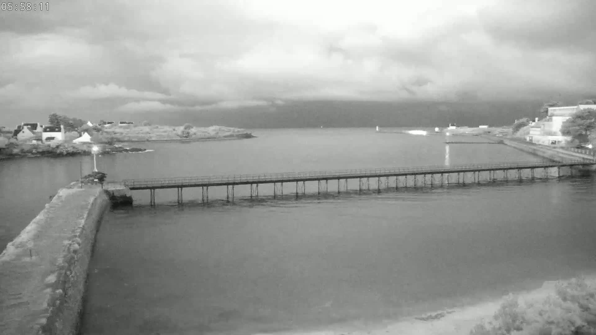 A long pier extends over calm water towards a small village under an overcast sky.