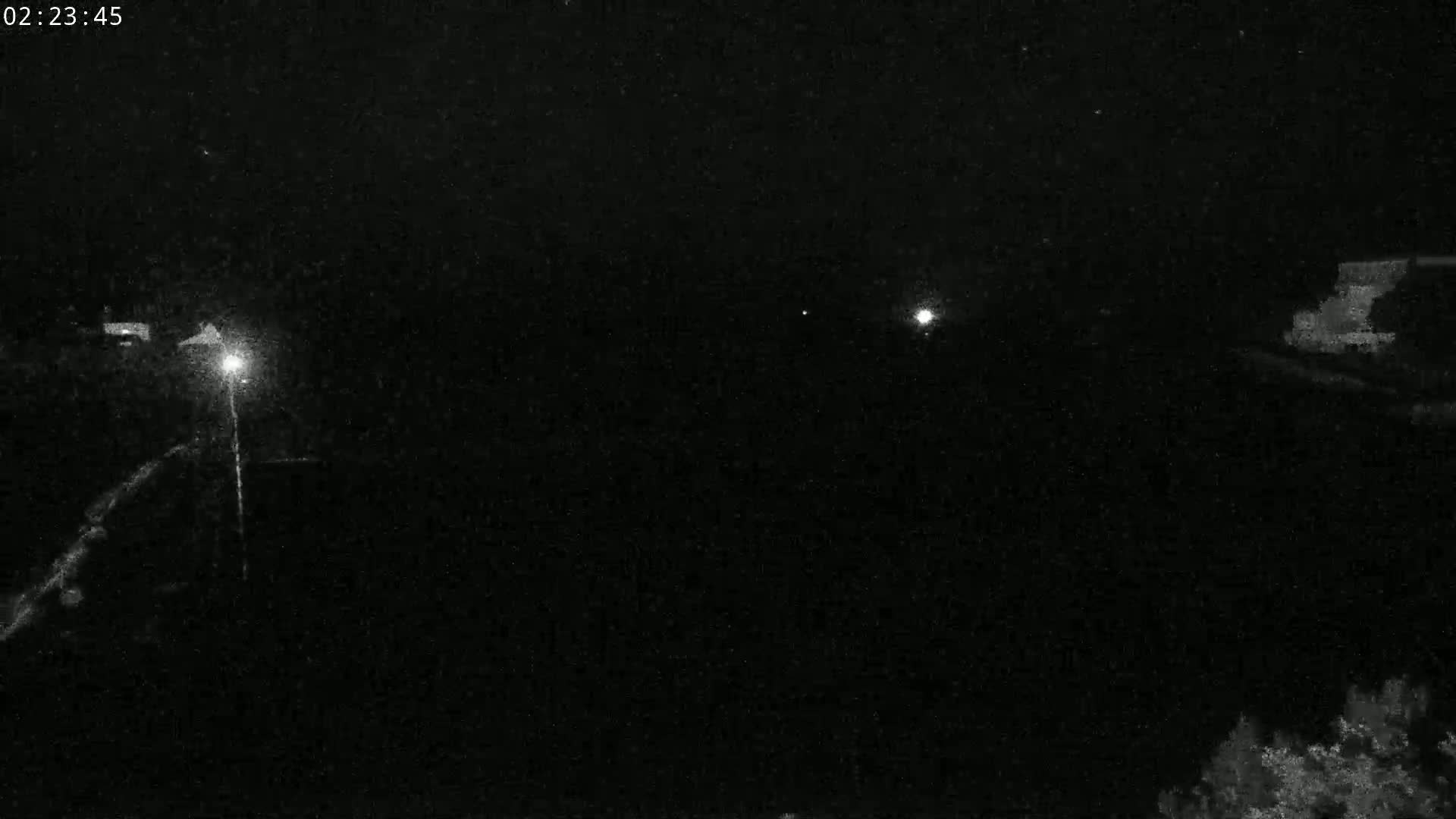 A nighttime, low-light view shows a dark road with faint light sources visible in the distance and some vegetation at the bottom right.