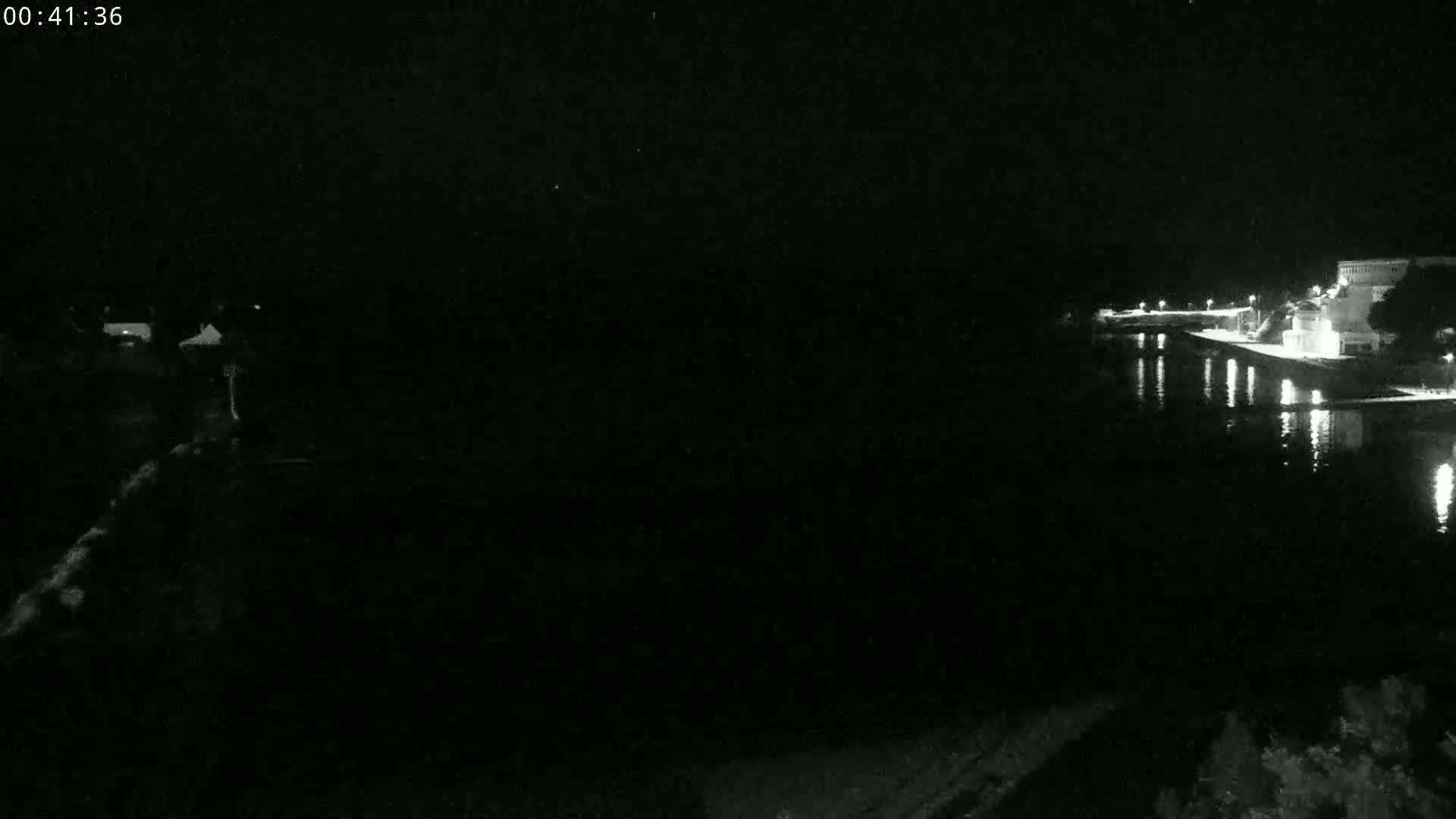 A nighttime view of a dark body of water reflecting lights from buildings on the opposite shore under a clear, starless sky.