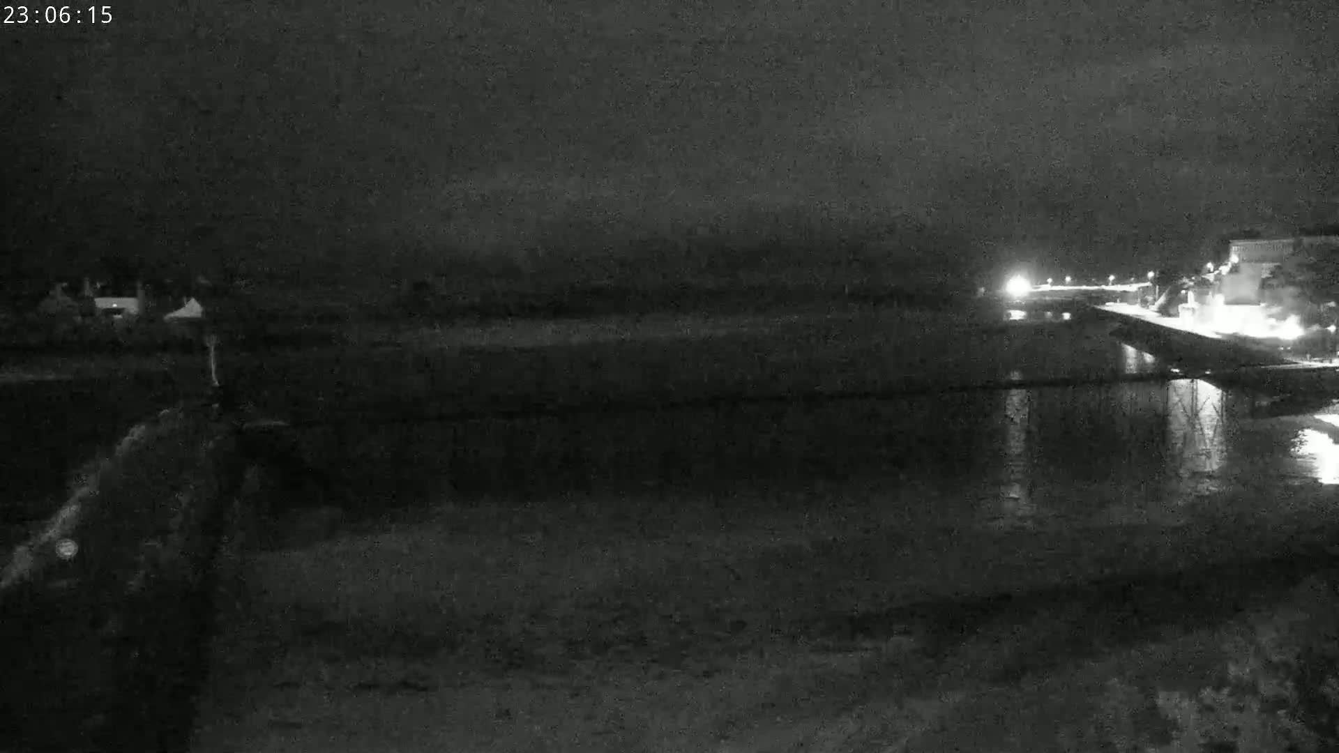 A nighttime, low-light view shows a dark body of water reflecting lights from a distant structure on the right.
