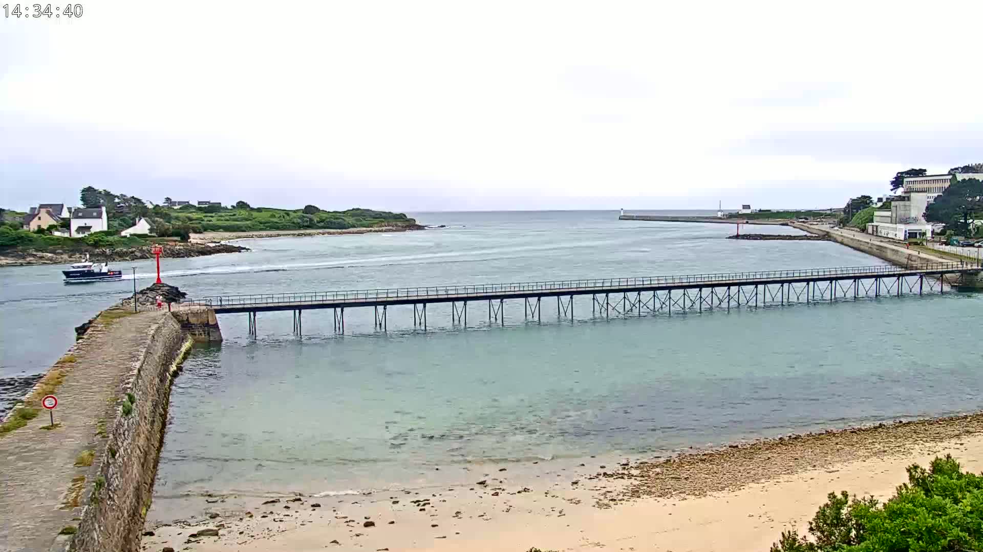 A long pier extends across calm, light-green water toward a distant shoreline under an overcast sky.