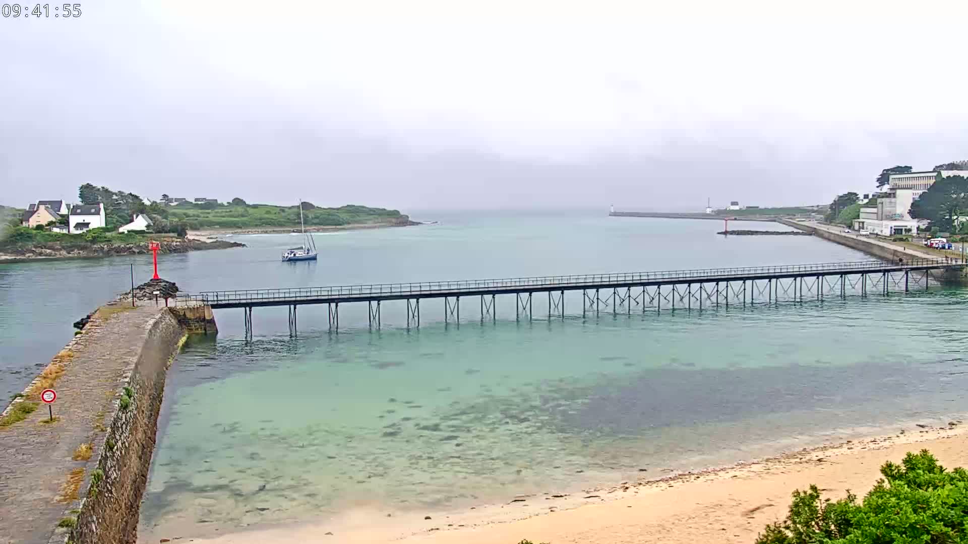 A long pier extends over clear, shallow water toward a small island on an overcast day.