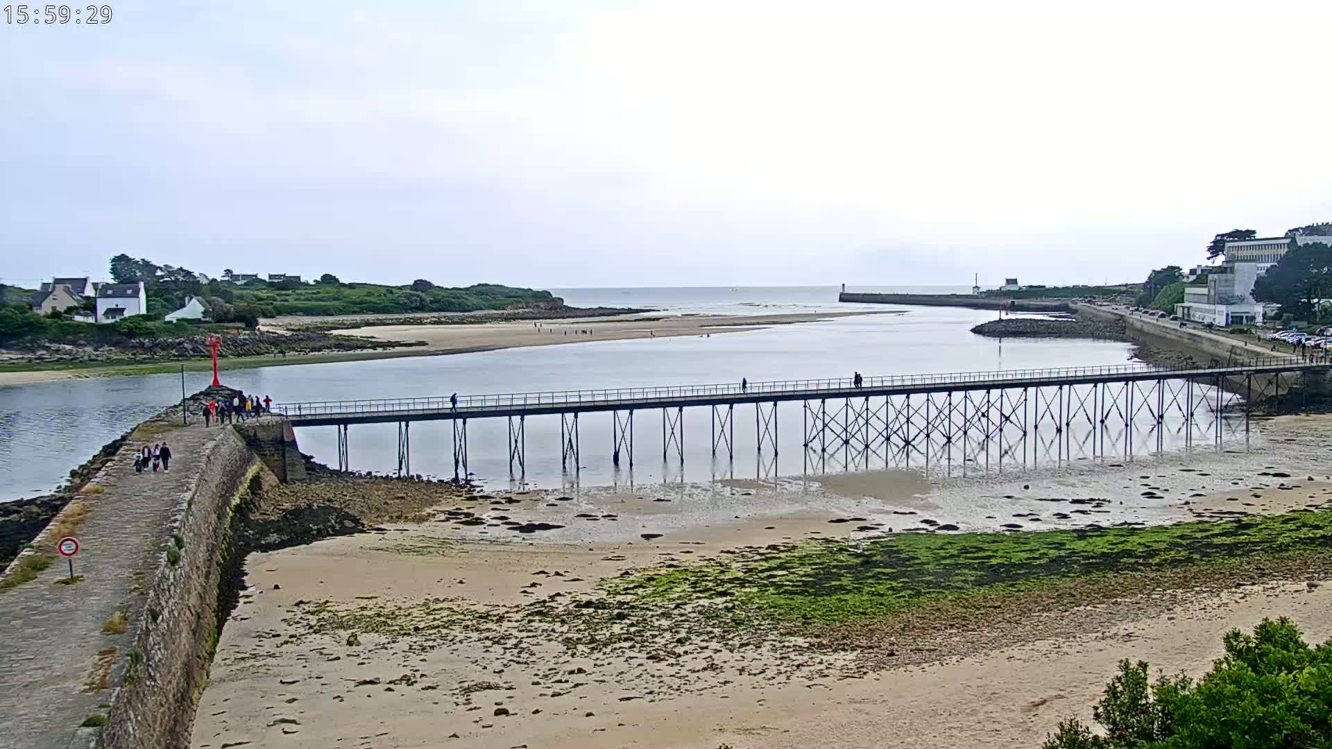 A long pier stretches across a calm body of water, connecting two shorelines under an overcast sky.