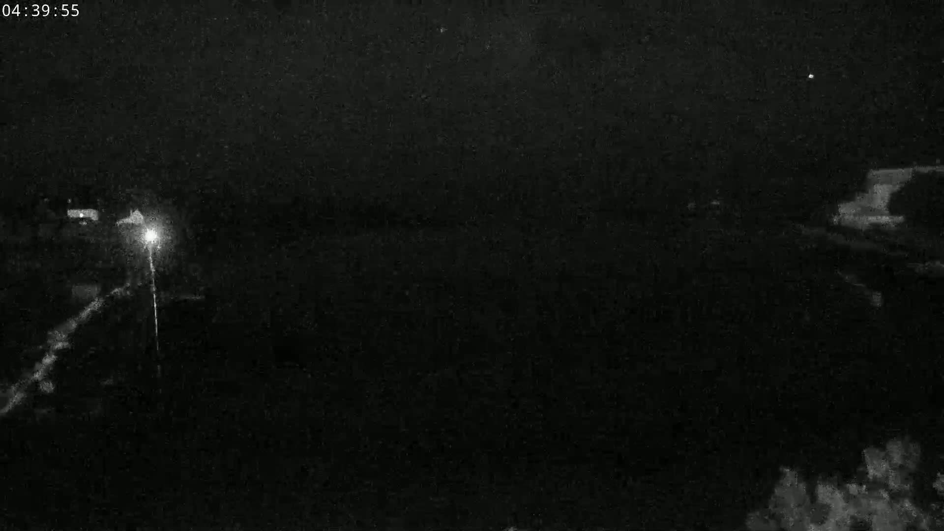 A nighttime, low-light image shows a dark, possibly rural landscape with a single bright light source visible in the distance.