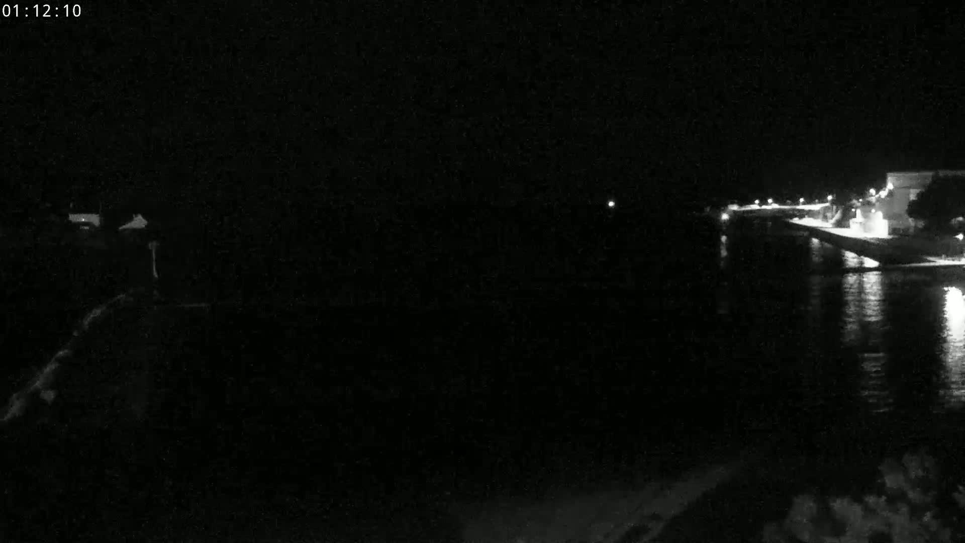 A nighttime, low-light image shows a dark body of water reflecting a few lights from a shoreline with buildings.