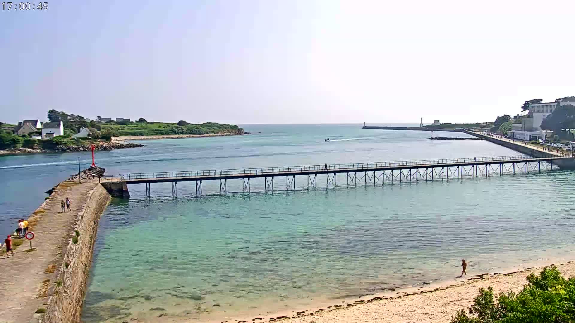 A long pier extends over clear, shallow water toward a small island on a sunny day.