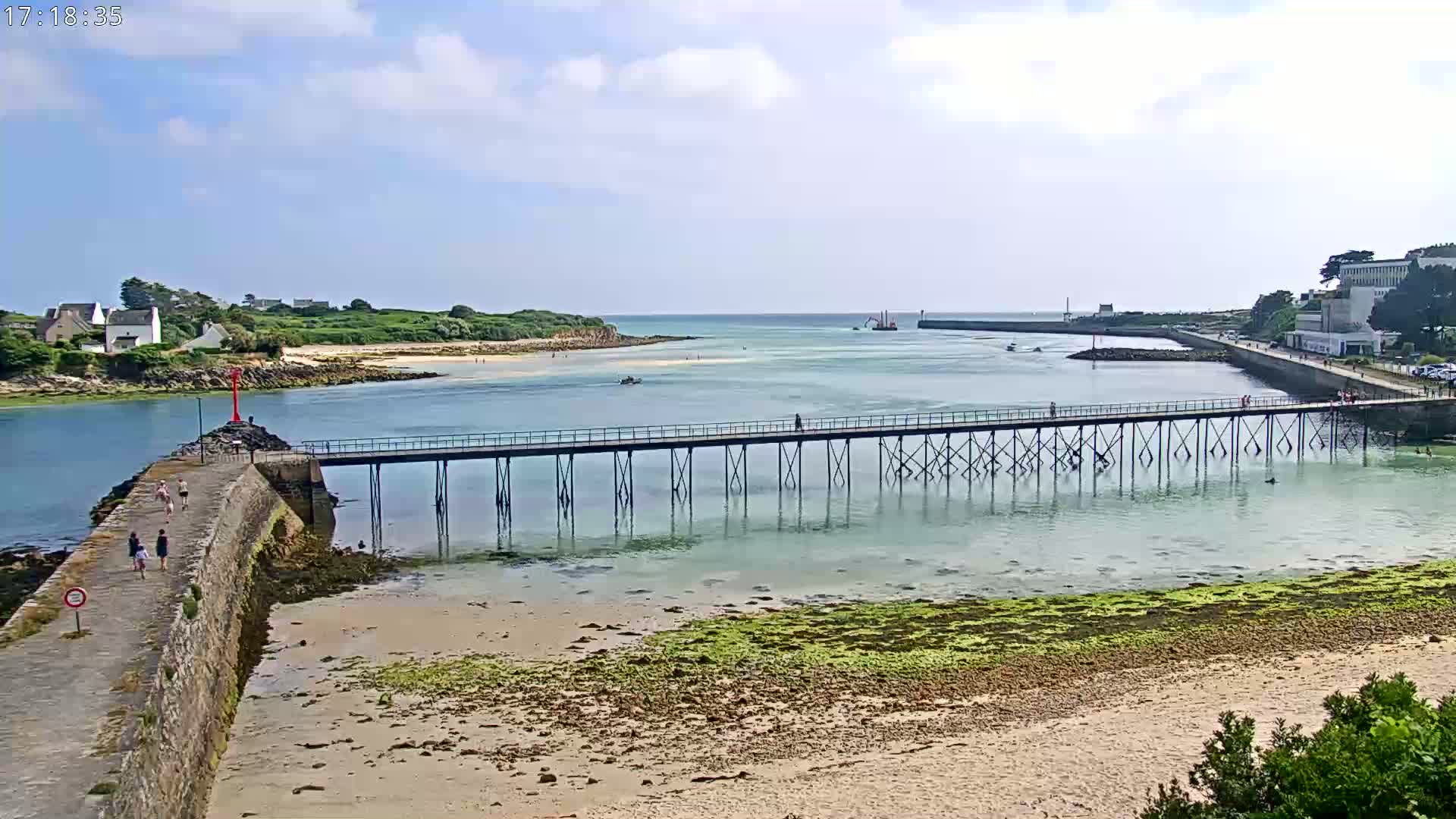 A long pier extends over calm, shallow water toward a small island under a partly cloudy sky.