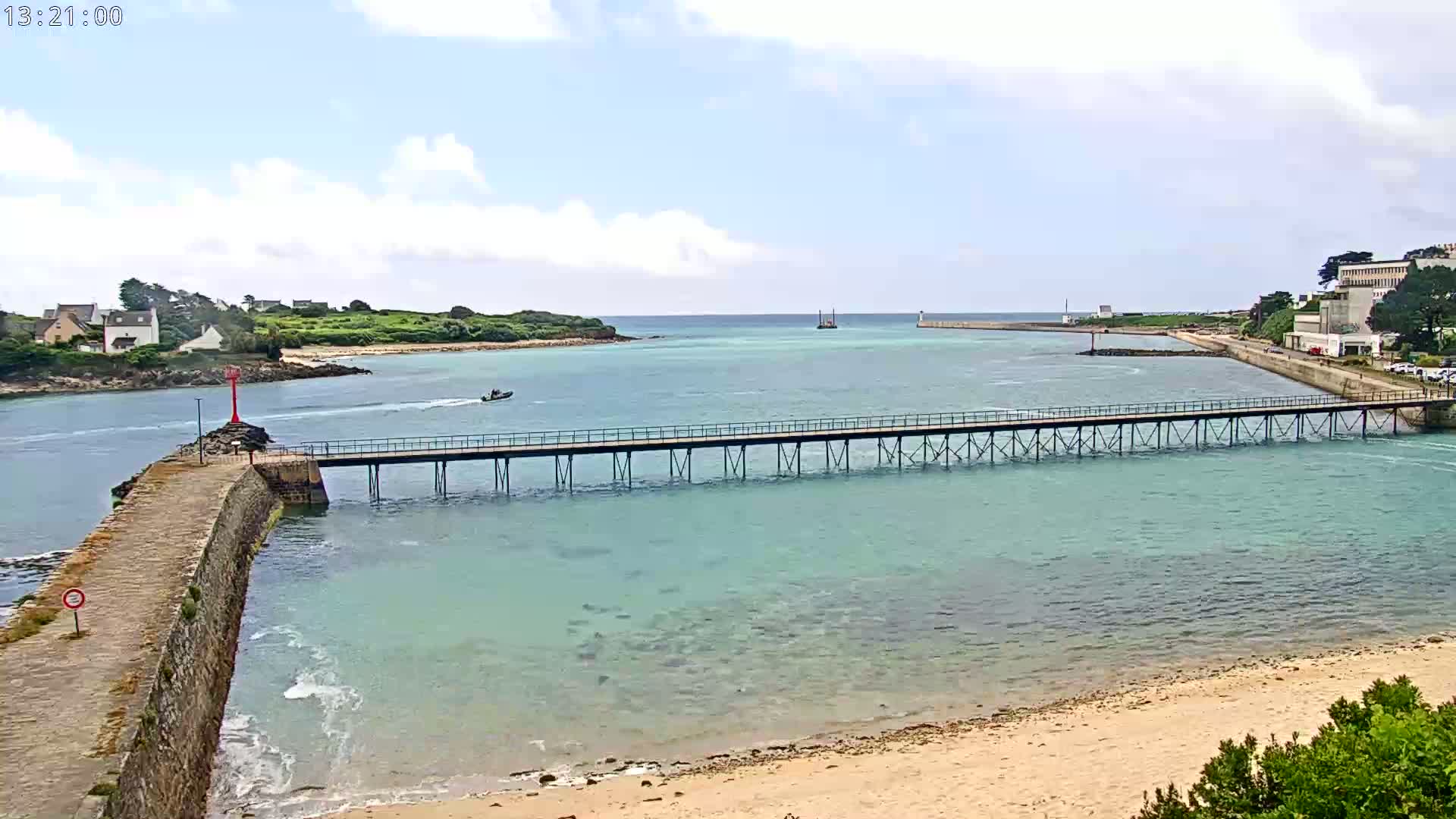 A long pier stretches across calm, light teal water towards a distant shoreline under a partly cloudy sky.