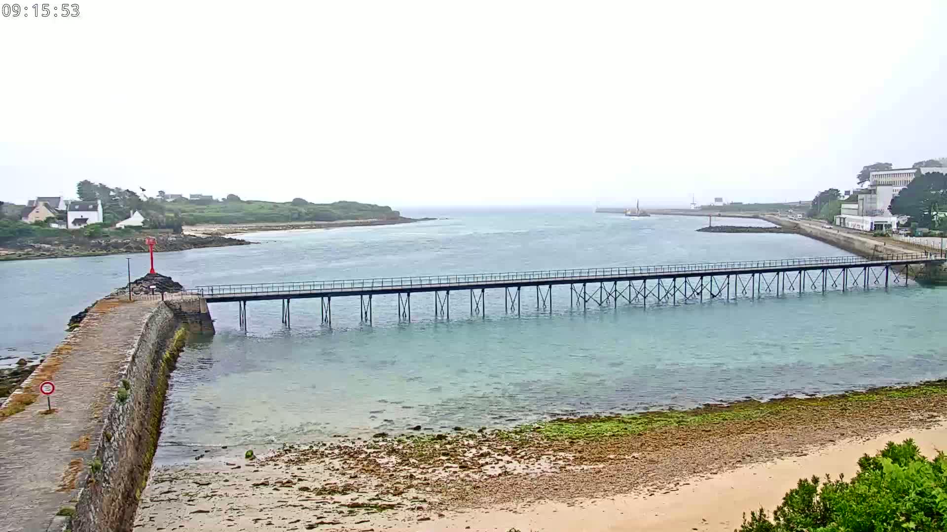 A long pier stretches across calm, light-blue water toward a distant shoreline on an overcast day.