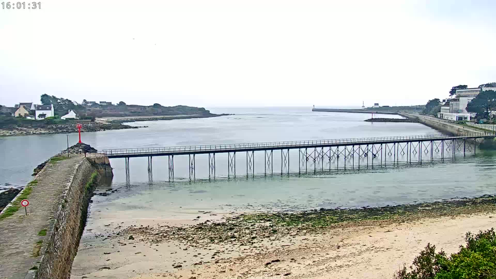 A long pier stretches across calm, shallow water toward a distant shoreline under an overcast sky.