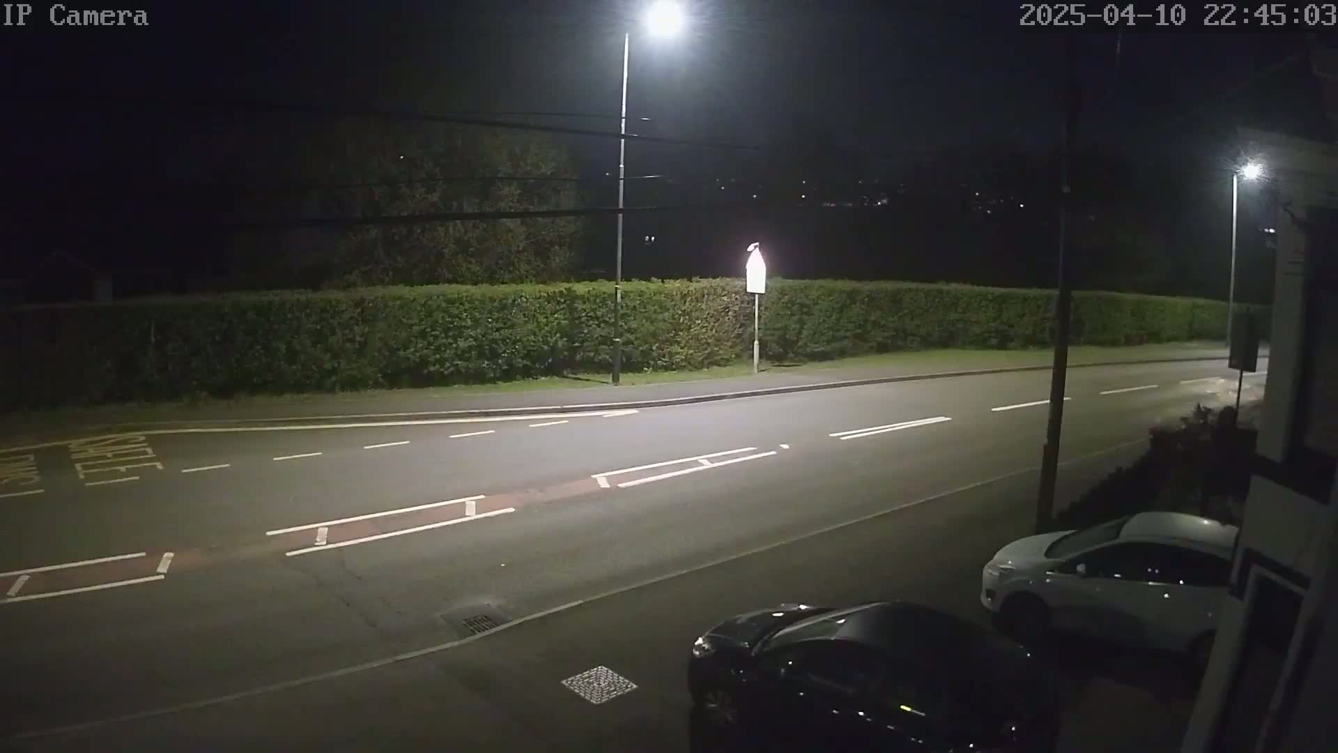 A nighttime street scene shows a road with white lane markings and parked cars under bright streetlights.