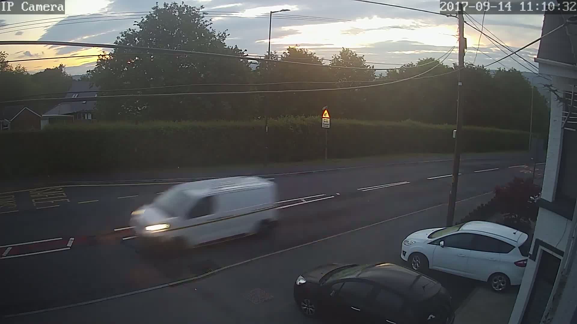 A white van and two cars are visible on a road at sunset under a partly cloudy sky.