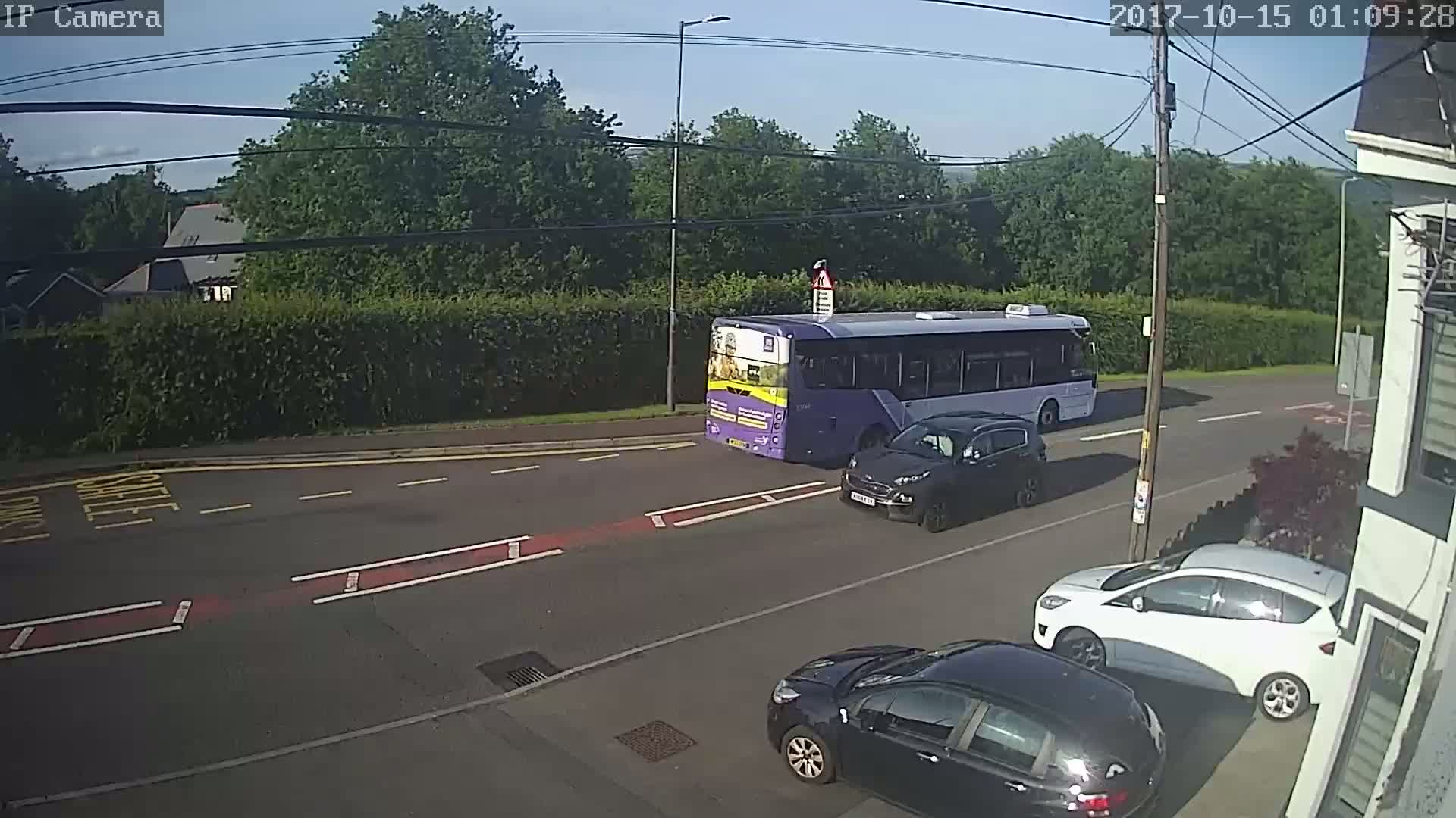 A purple bus and several cars are on a road under a mostly sunny sky.