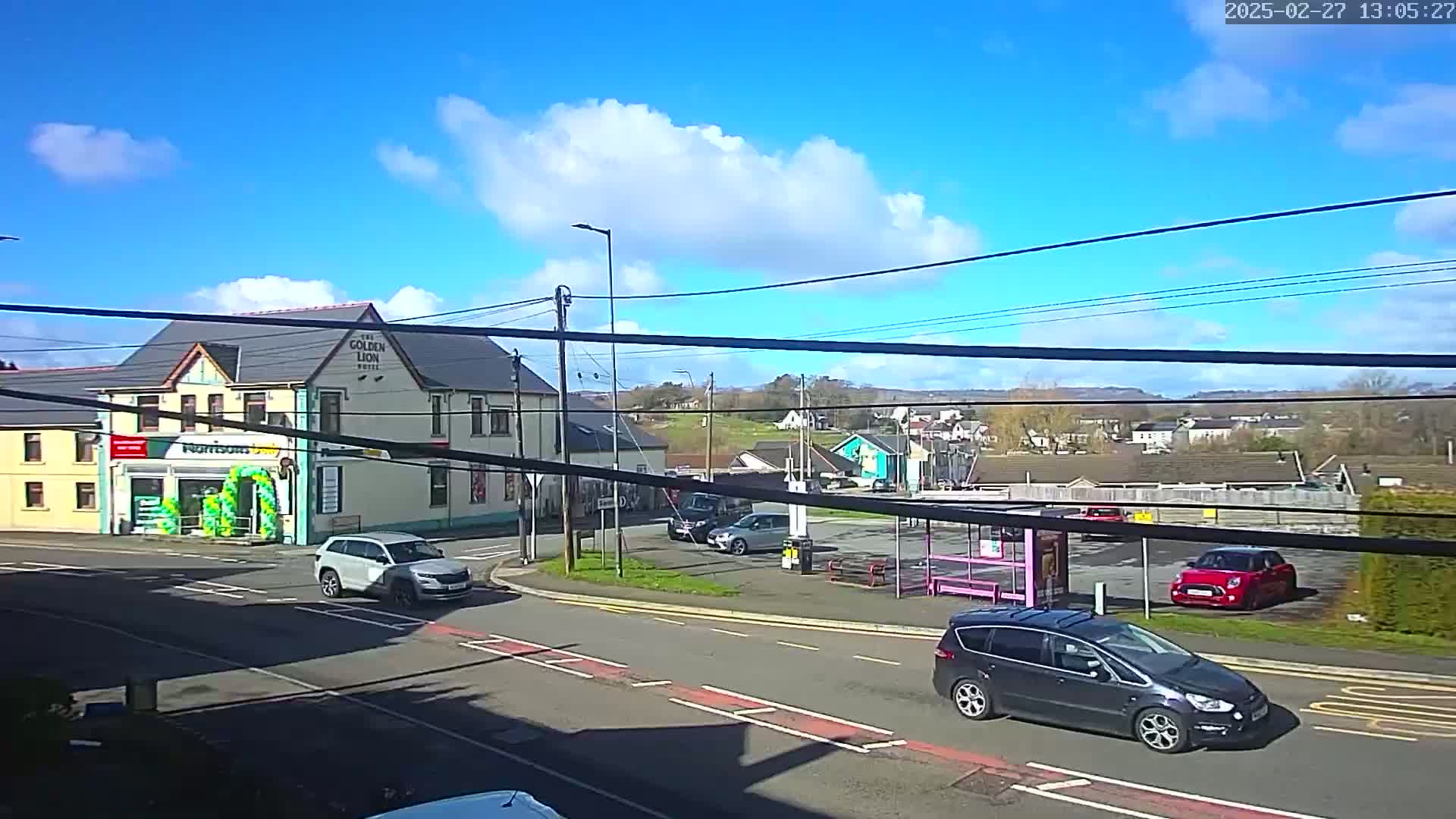 A sunny day reveals a street scene with several cars, a pub called "The Golden Lion Hotel," and a small parking lot, all situated near a crossroad.