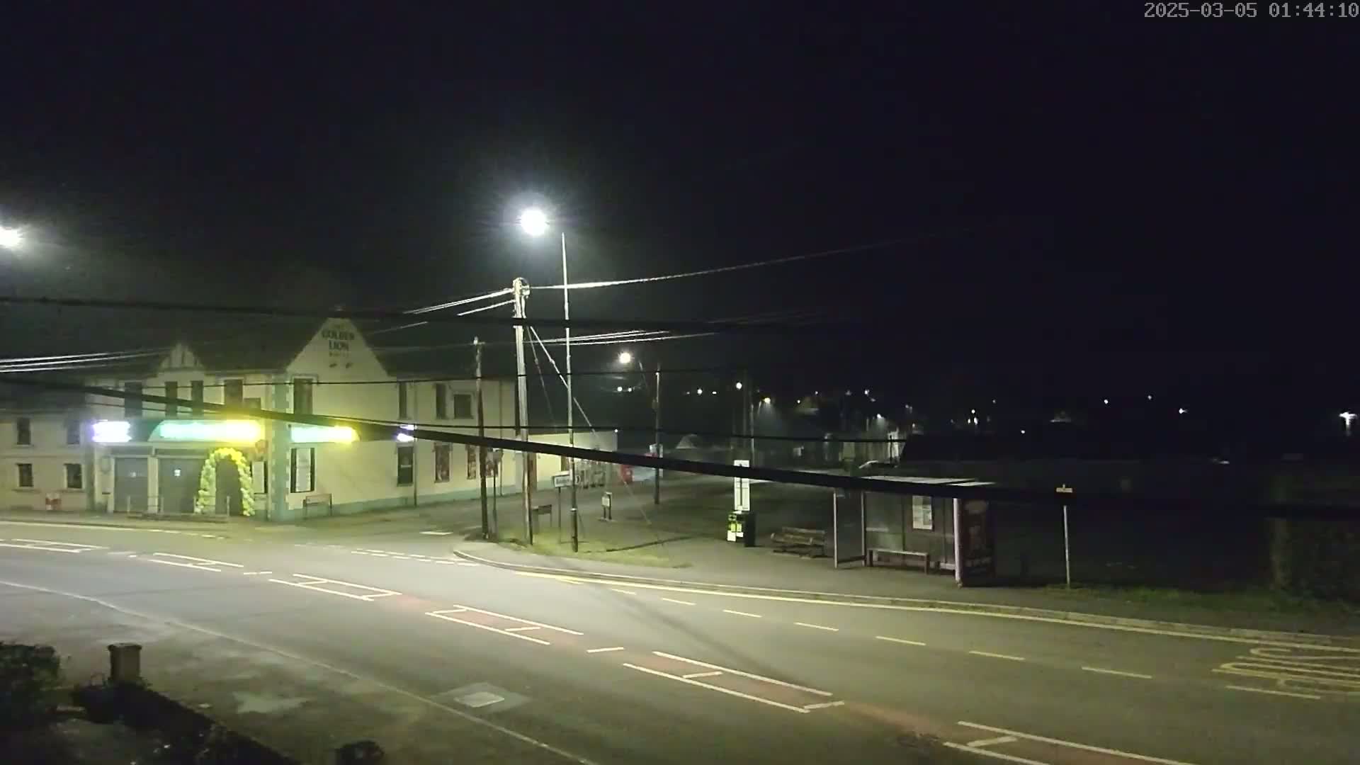 A nighttime street scene shows a pub, a bus stop, and a sparsely lit road under a dark sky.