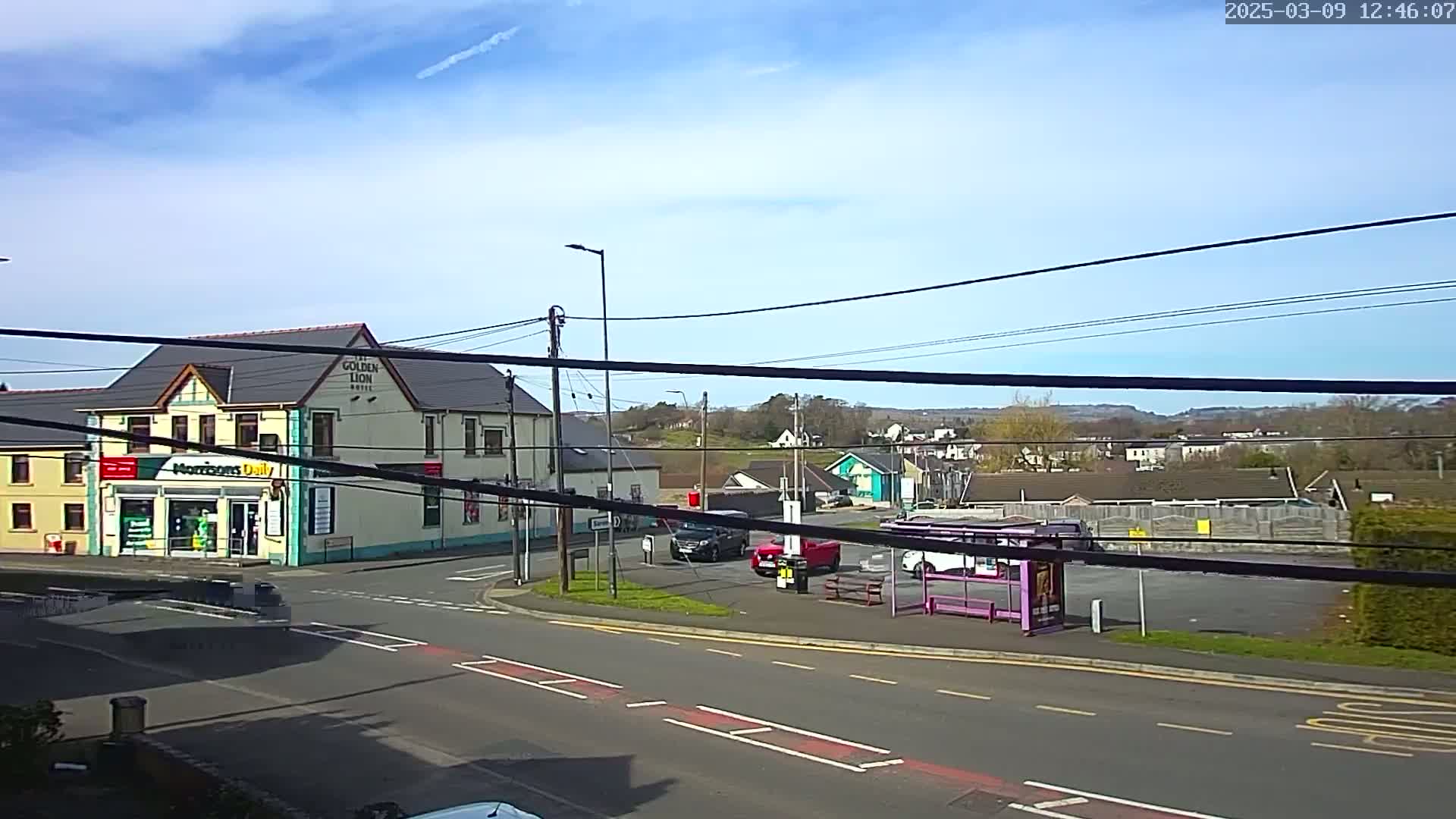 A street intersection with a pub, a small convenience store, a bus stop, several cars, and a partly sunny sky is visible.