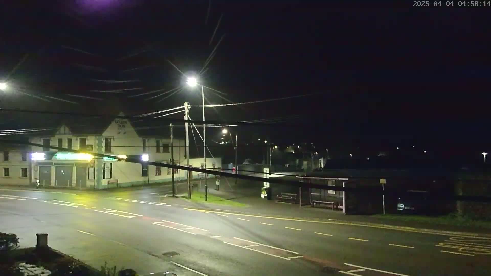 A nighttime street scene shows a building with a bus stop across the road under dark, clear skies.
