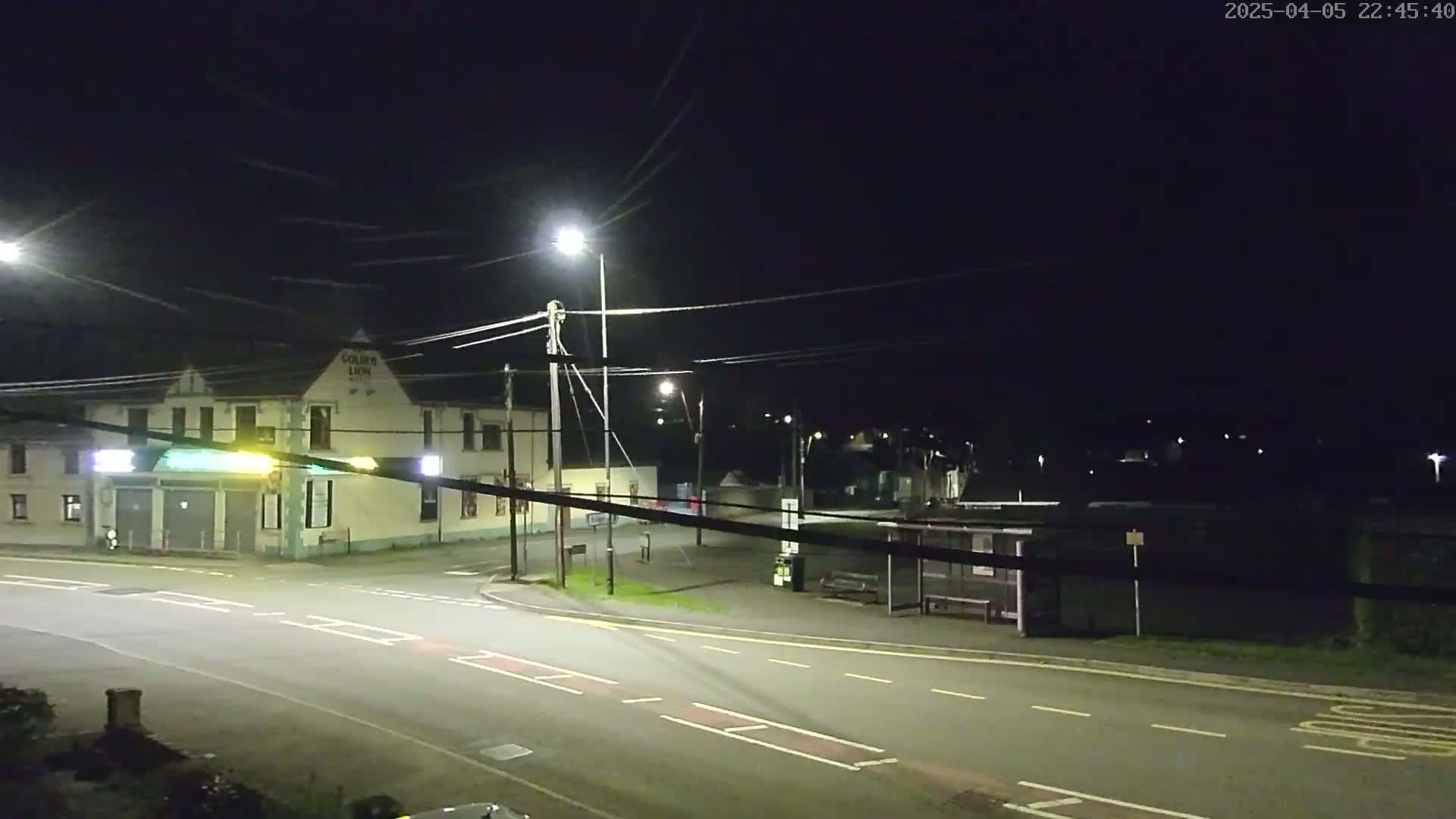 A nighttime street scene shows a building, a bus stop, and a road intersection illuminated by streetlights under a clear, dark sky.