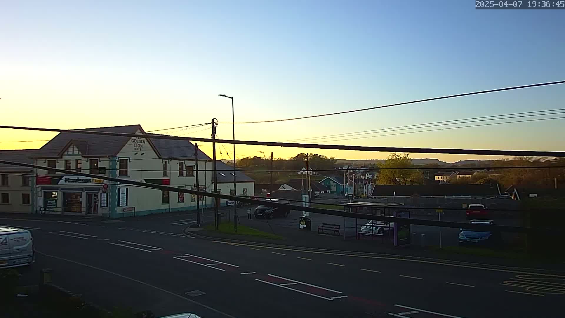 A two-story building with a shop on the ground floor sits at a road intersection under a twilight sky.
