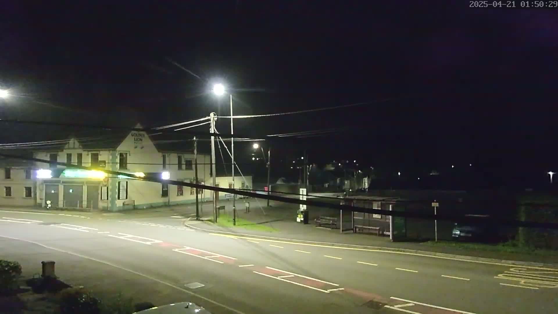 A nighttime street scene shows a pub, a bus stop, and a roadway intersection under artificial street lighting.
