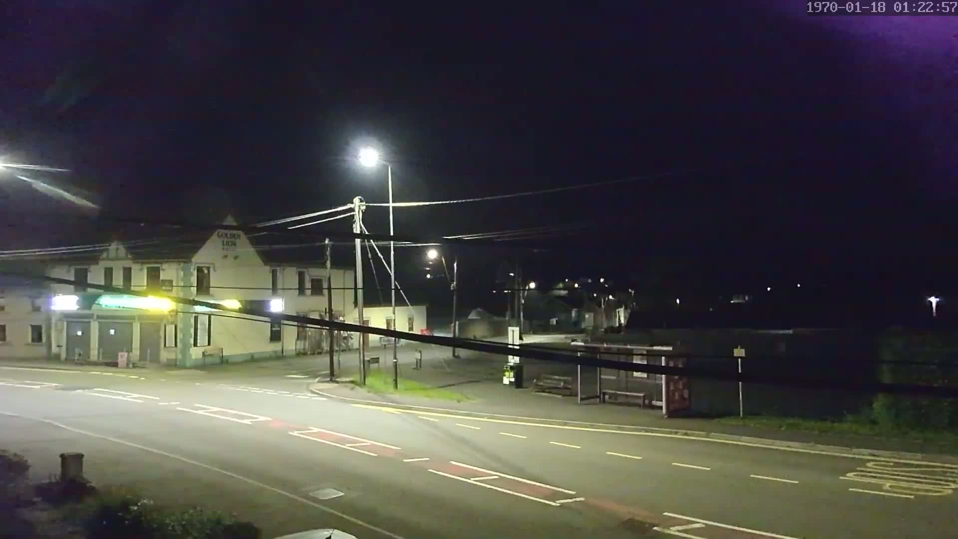 A nighttime street scene shows a crossroads with a pub, a bus stop, and streetlights under a dark, clear sky.