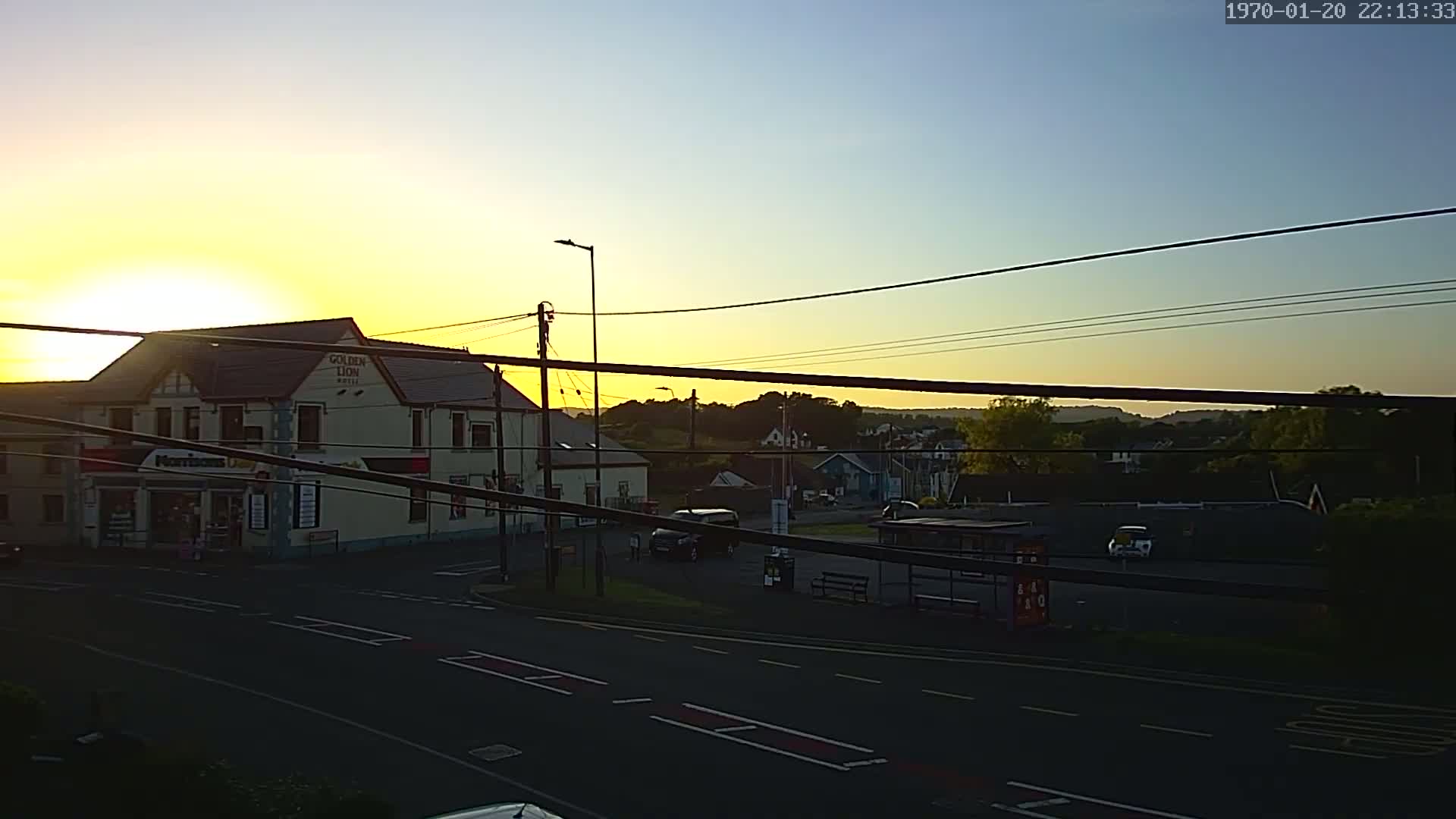 A two-story building sits on a corner near a road at sunset, with other buildings and trees visible in the background under a clear sky.