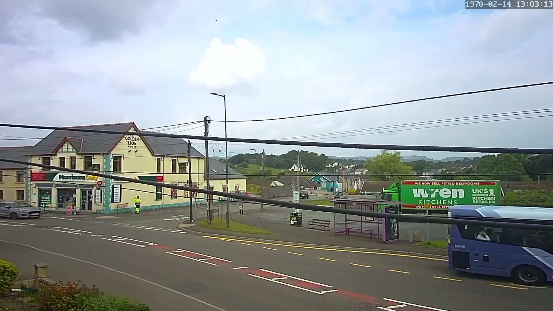 A mostly cloudy day reveals a street scene with a pub, a small shop, a bus stop, and a large bus.