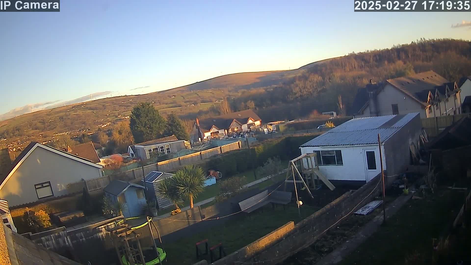 A backyard scene with houses and a hilly landscape in the background under a clear, bright sky.