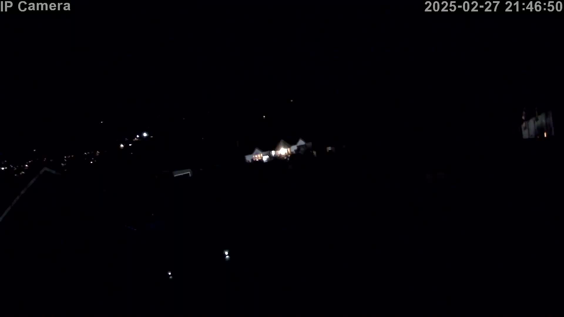 A dimly lit structure is visible in the dark, possibly at night, with some other faint lights scattered in the distance.