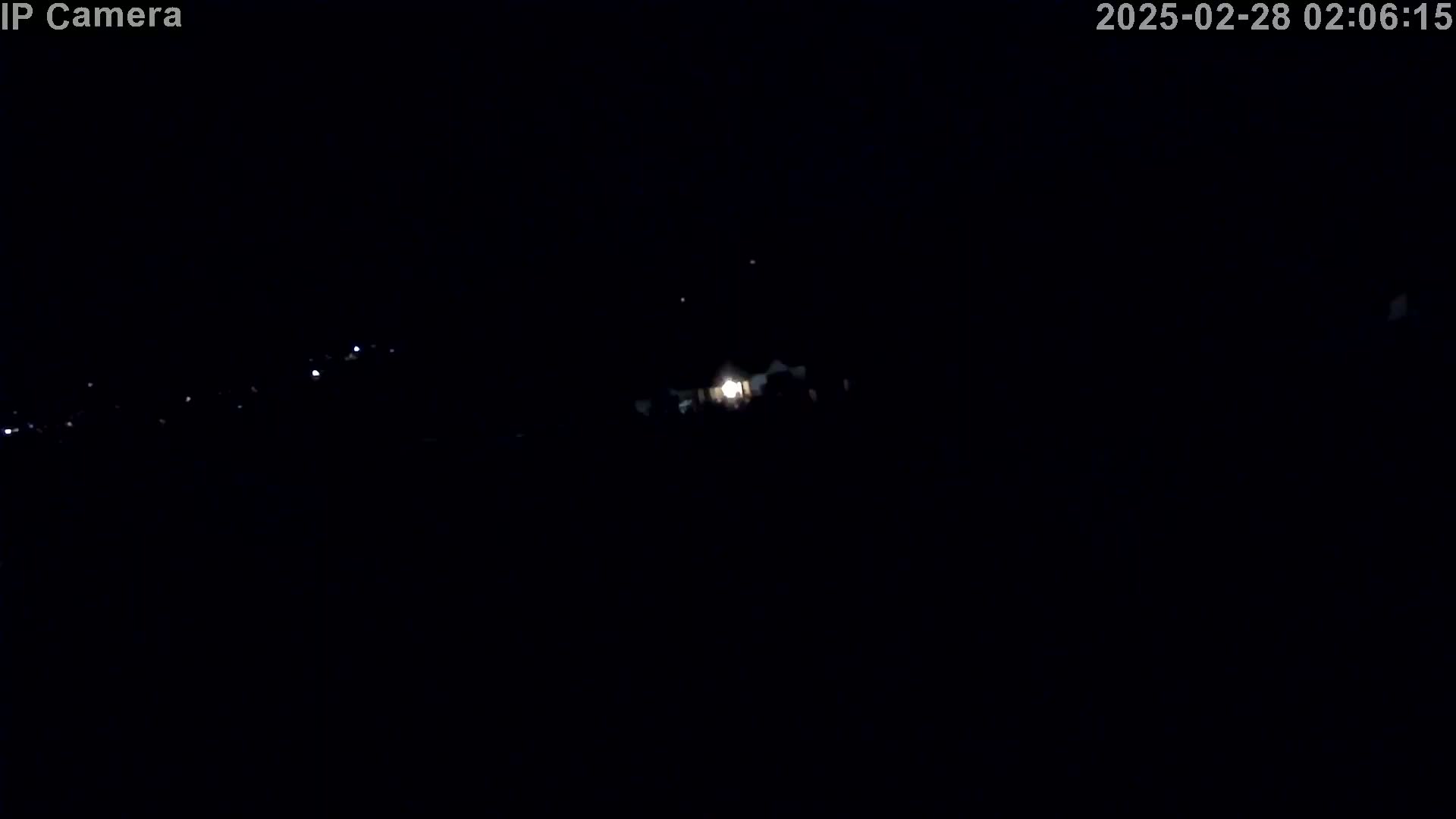 A dimly lit nighttime scene shows a few distant lights and a brighter light source in the center.