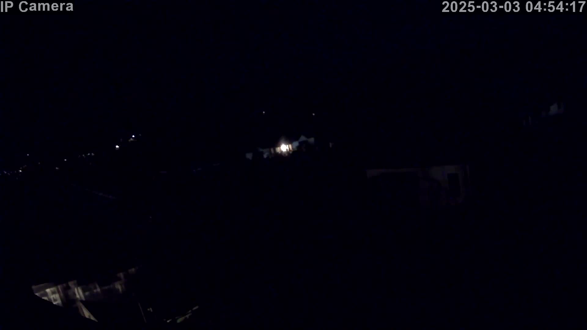 A nighttime, outdoor view shows faintly illuminated structures and distant lights under a dark sky.